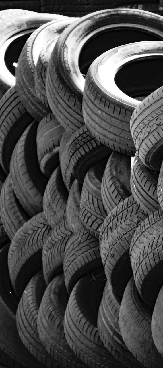 Pile of used tires stacked in a pattern; monochrome.