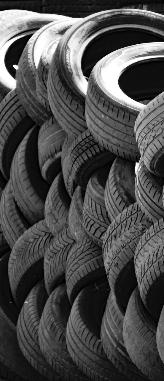 Pile of used tires stacked in a pattern; monochrome.