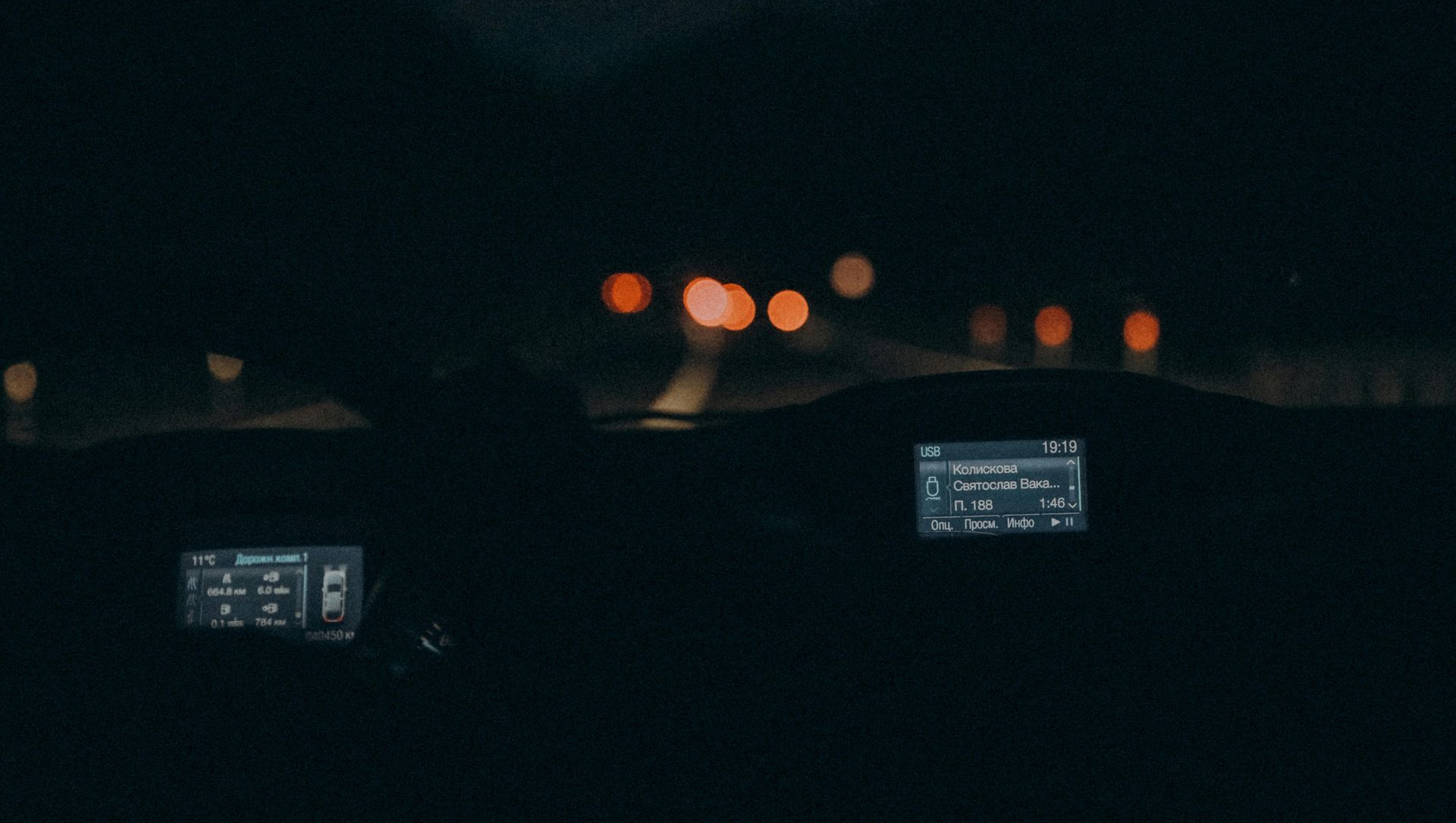 Interior car view at night, headlights ahead with blurry orange lights.