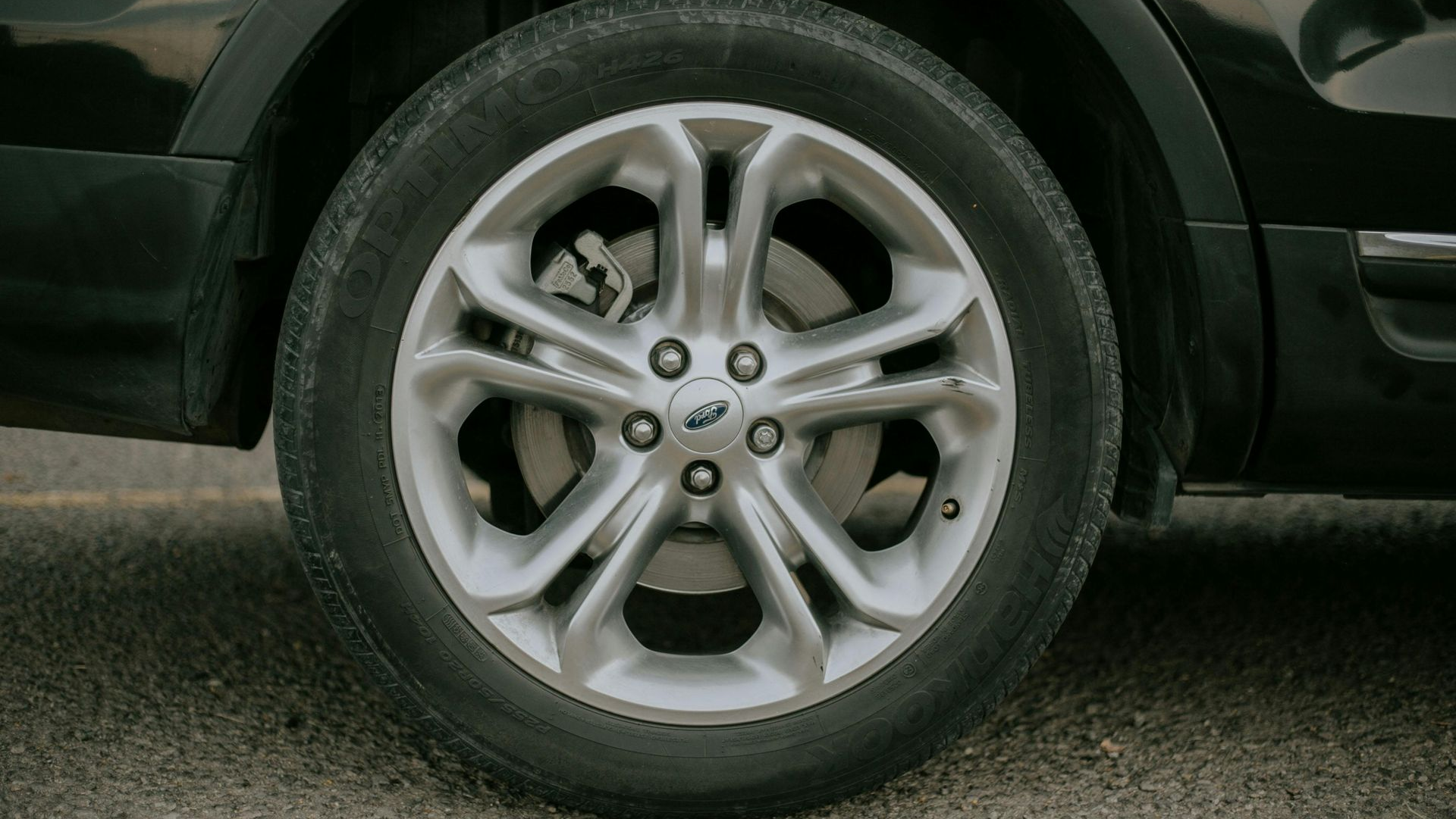 Close-up of a silver car wheel with a black tire on asphalt.