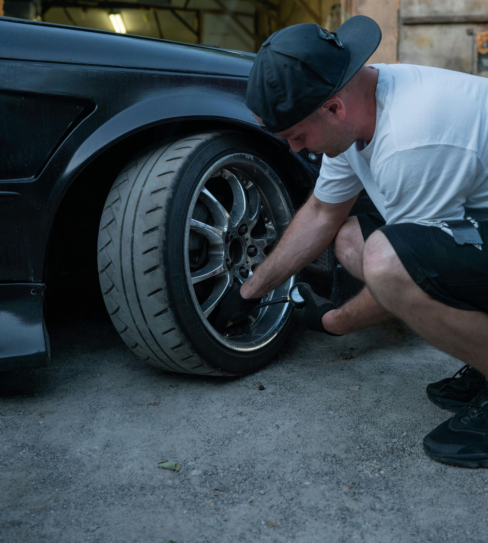 Man kneeling by black car's tire, adjusting it outdoors.