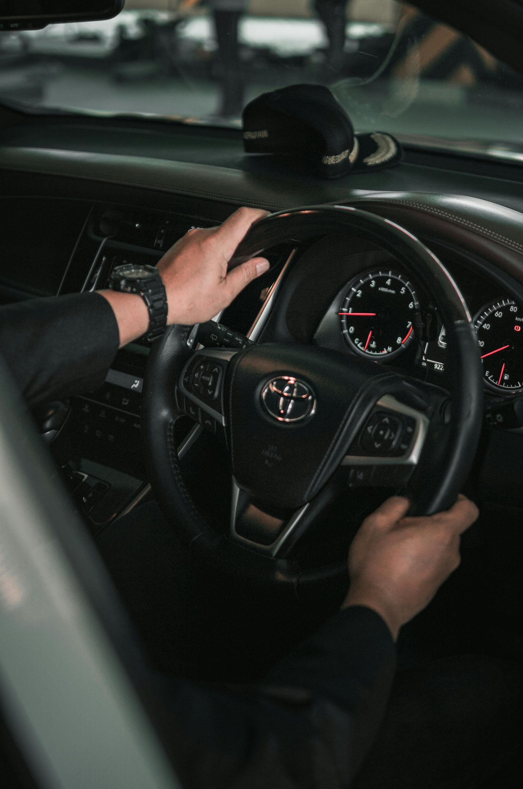 Hands gripping a black steering wheel inside a Toyota car, dashboard visible.