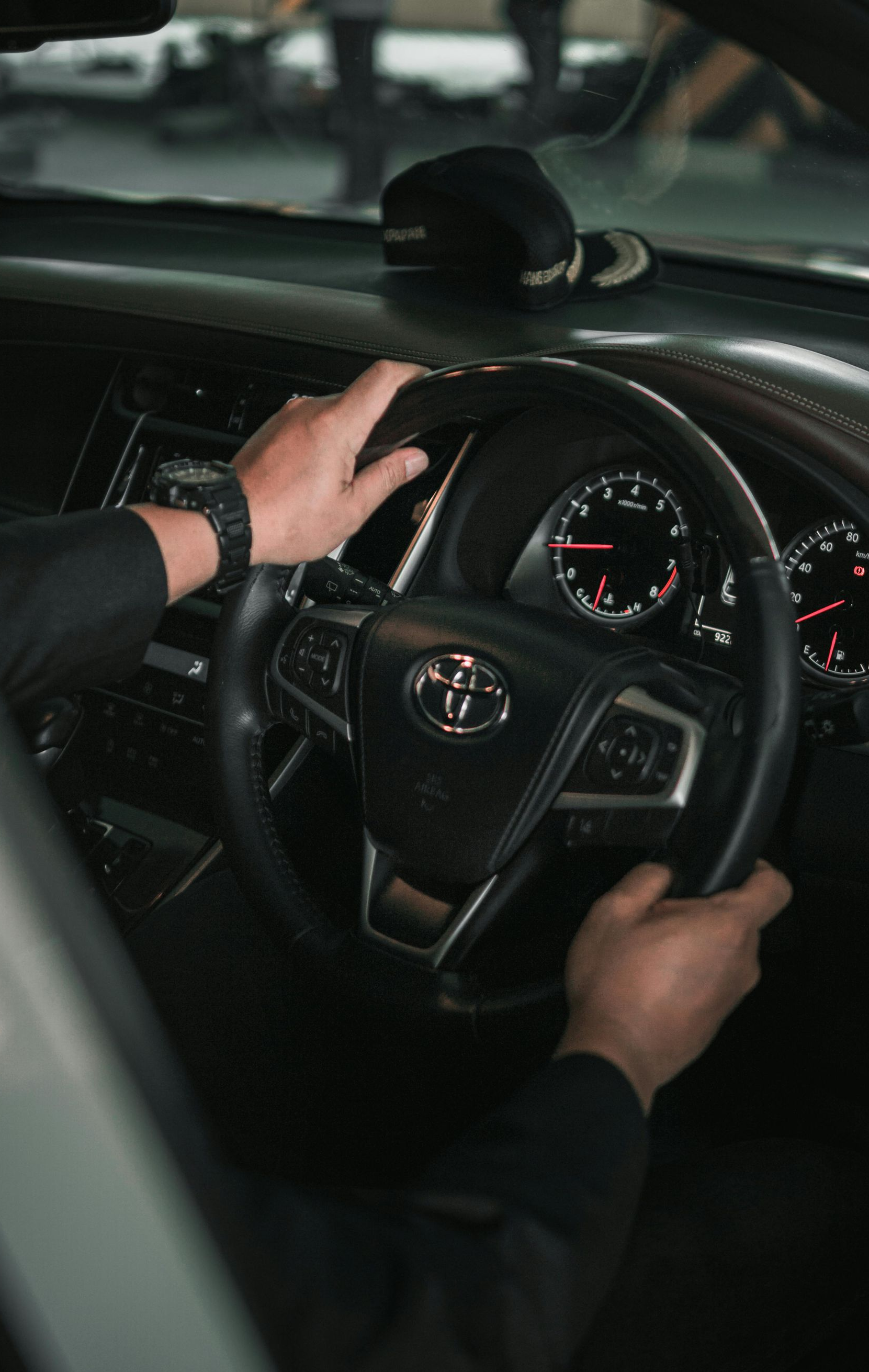 Hands gripping a black steering wheel inside a Toyota car, dashboard visible.