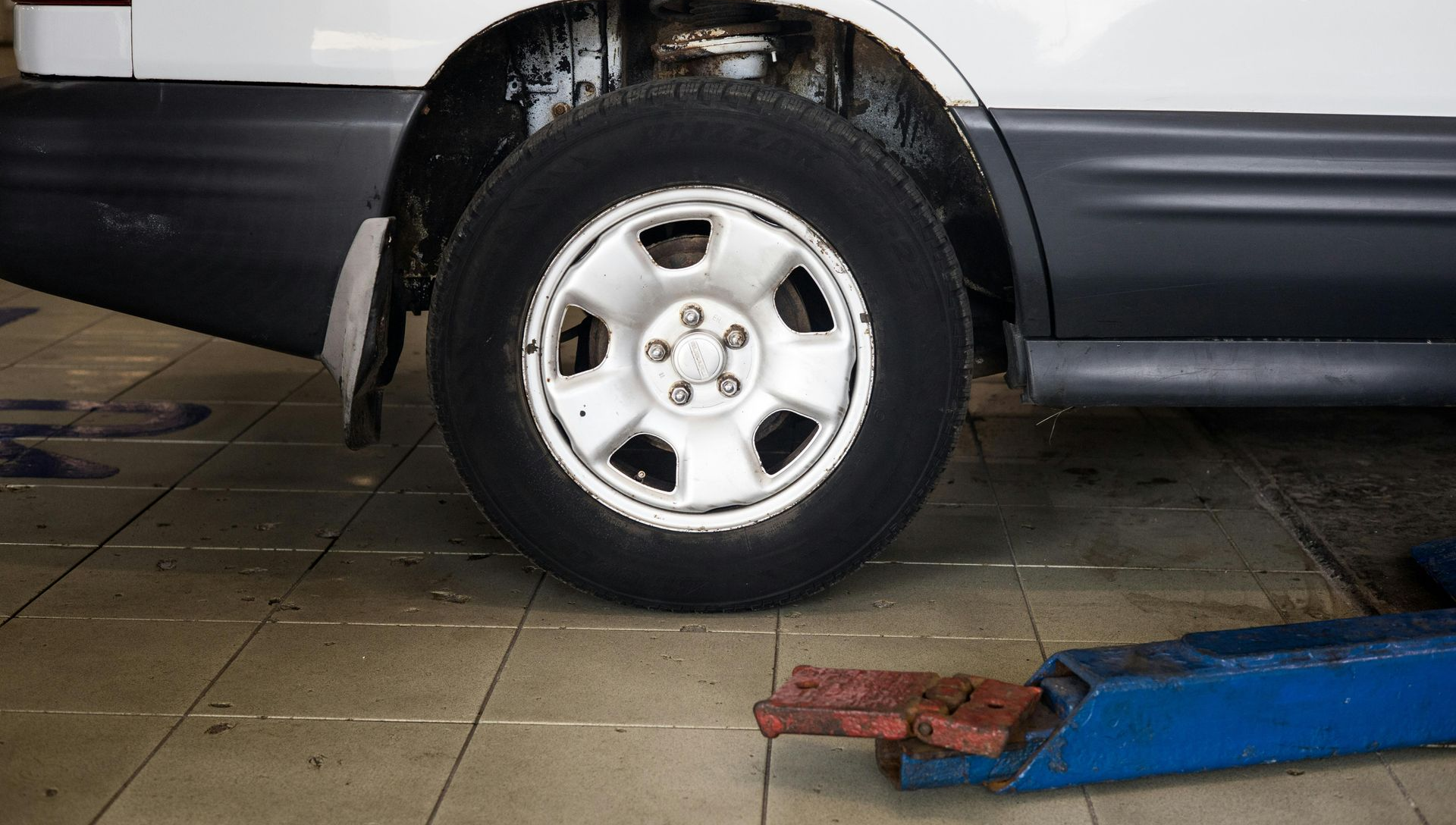 White car with rear tire removed, in a garage.