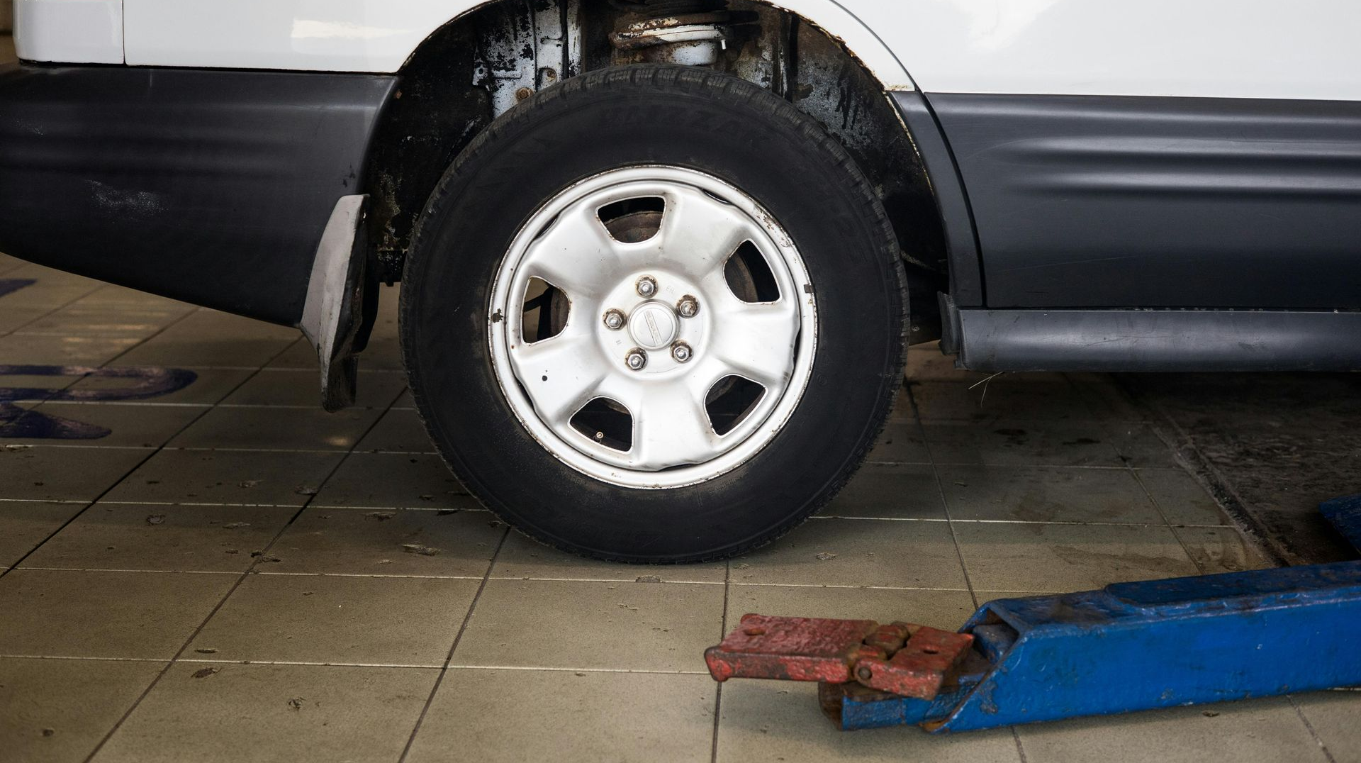 White car tire on a light gray rim in a repair shop, next to a blue lift.
