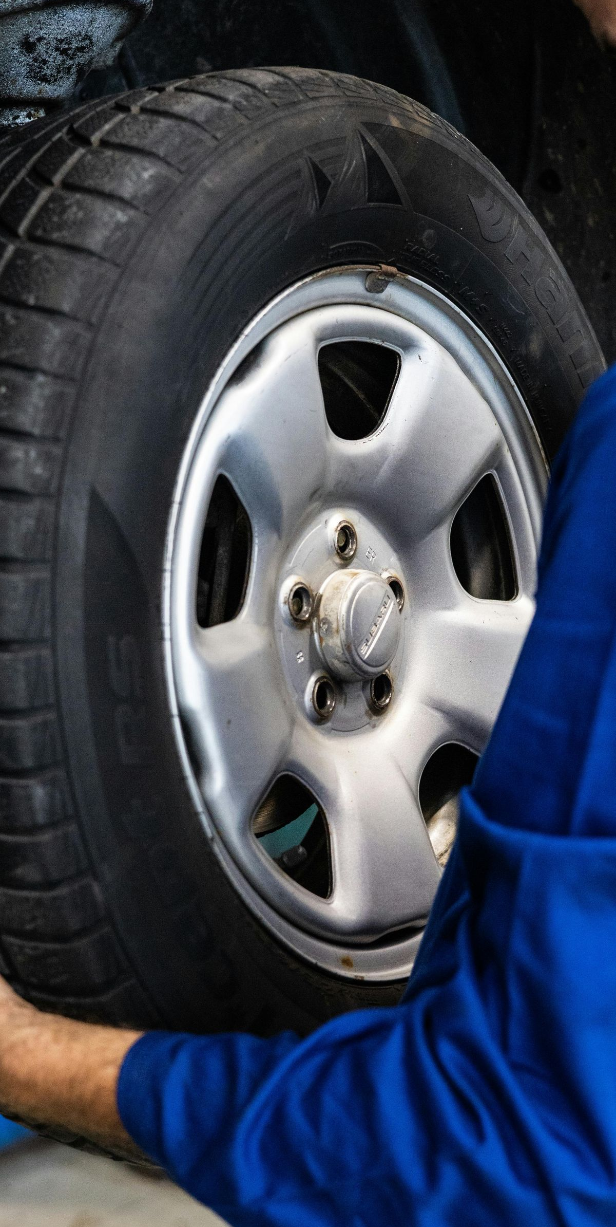 A person in blue holding a car tire. The tire is black and the rim is silver.