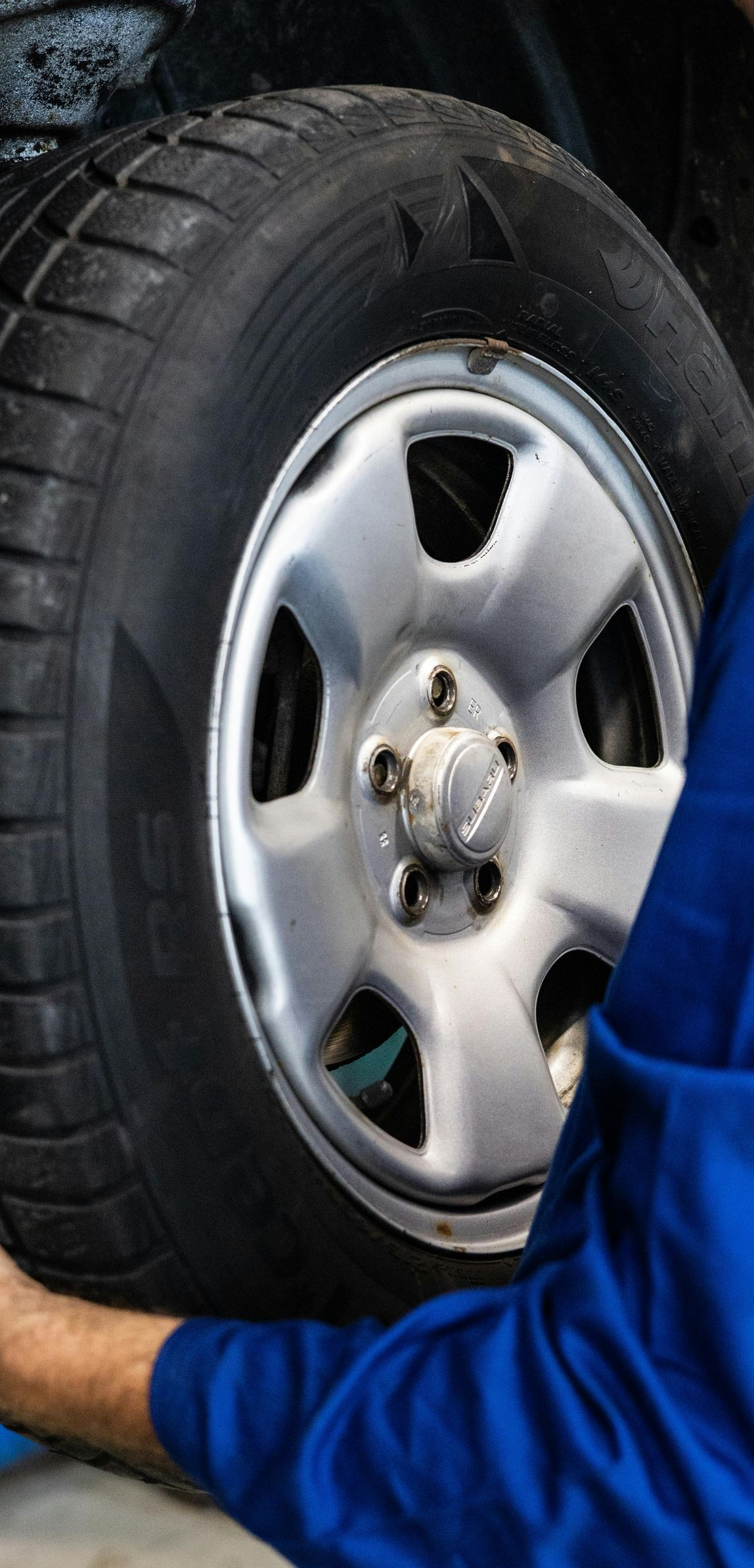A person in blue holding a car tire. The tire is black and the rim is silver.
