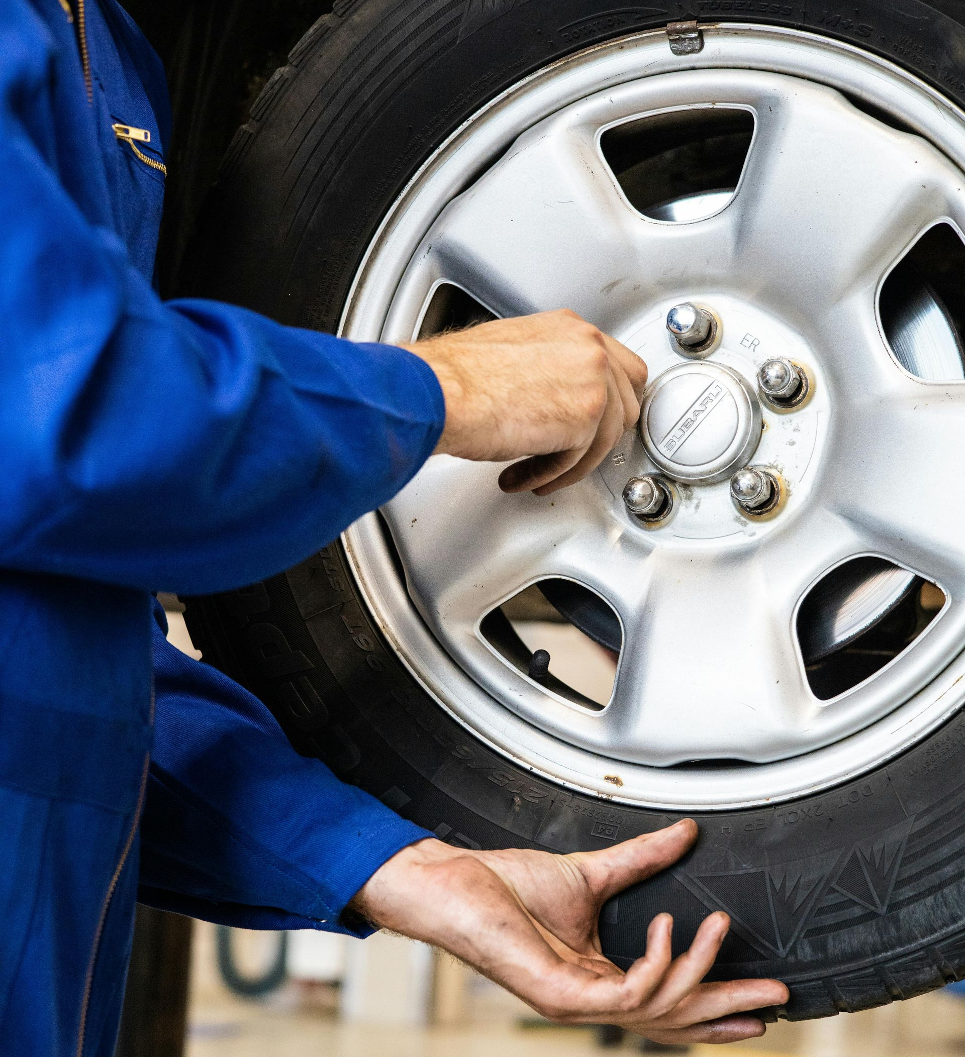 Mechanic in blue coveralls changing a car tire, hands on wheel and hubcap.