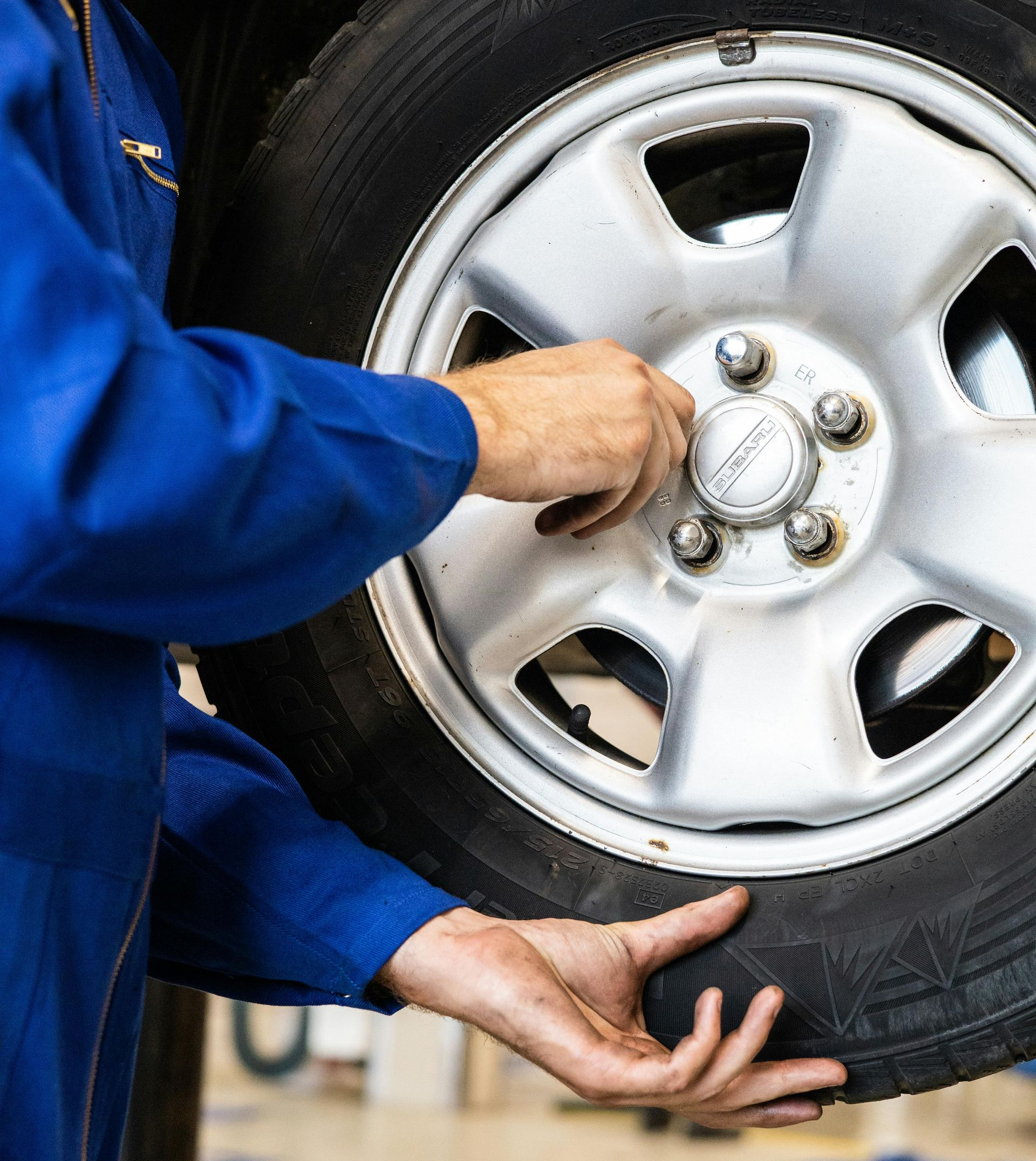 Person in blue jumpsuit working on a car tire, tightening lug nuts.