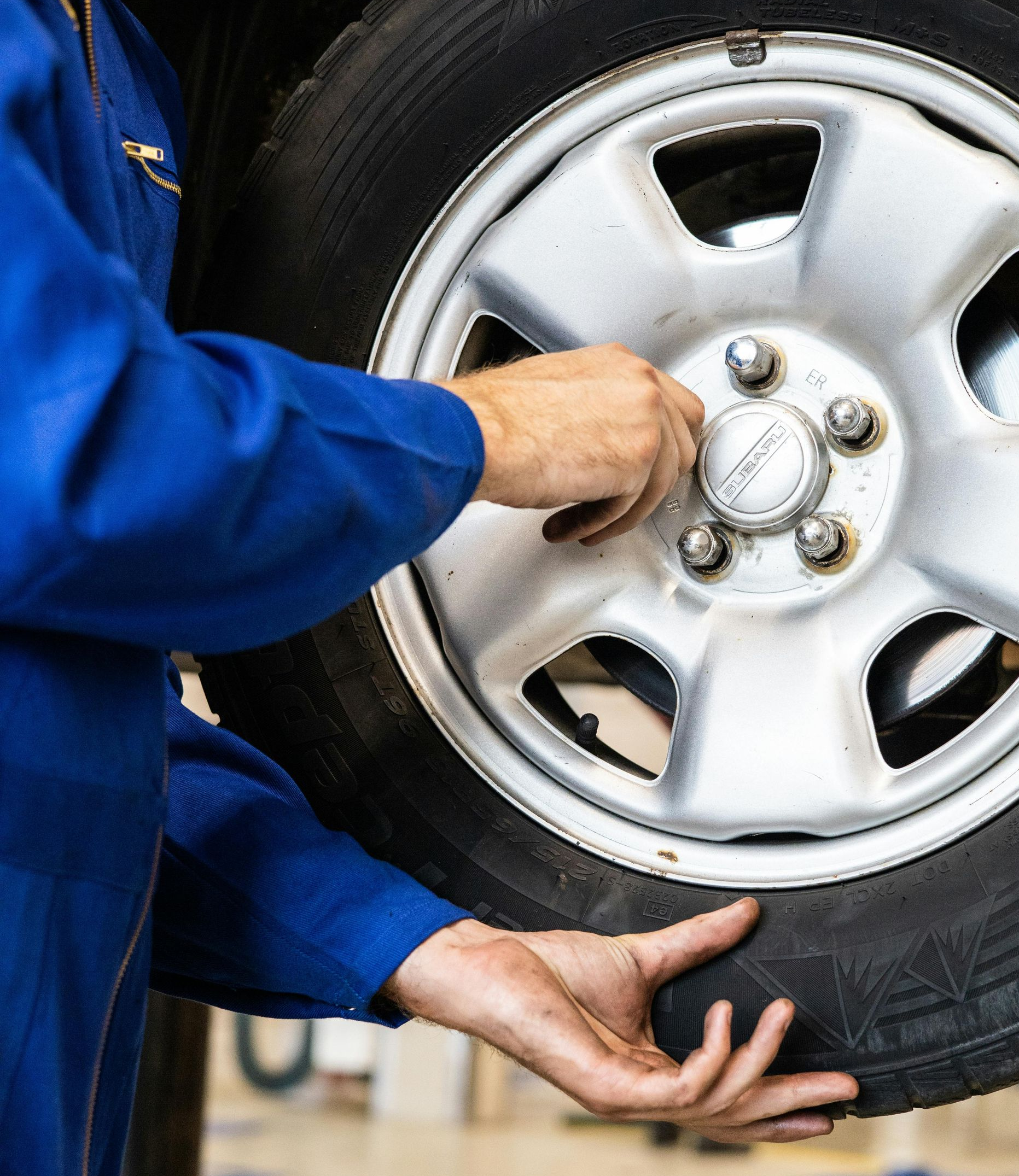 Person in blue jumpsuit working on a car tire, tightening lug nuts.