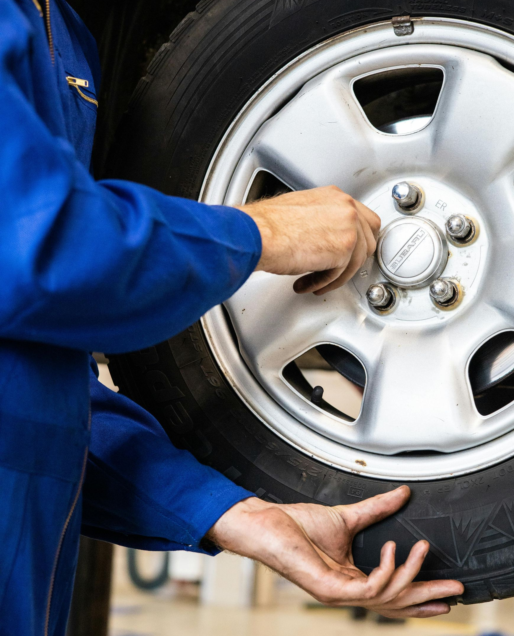 Person in blue jumpsuit working on a car tire, tightening lug nuts.