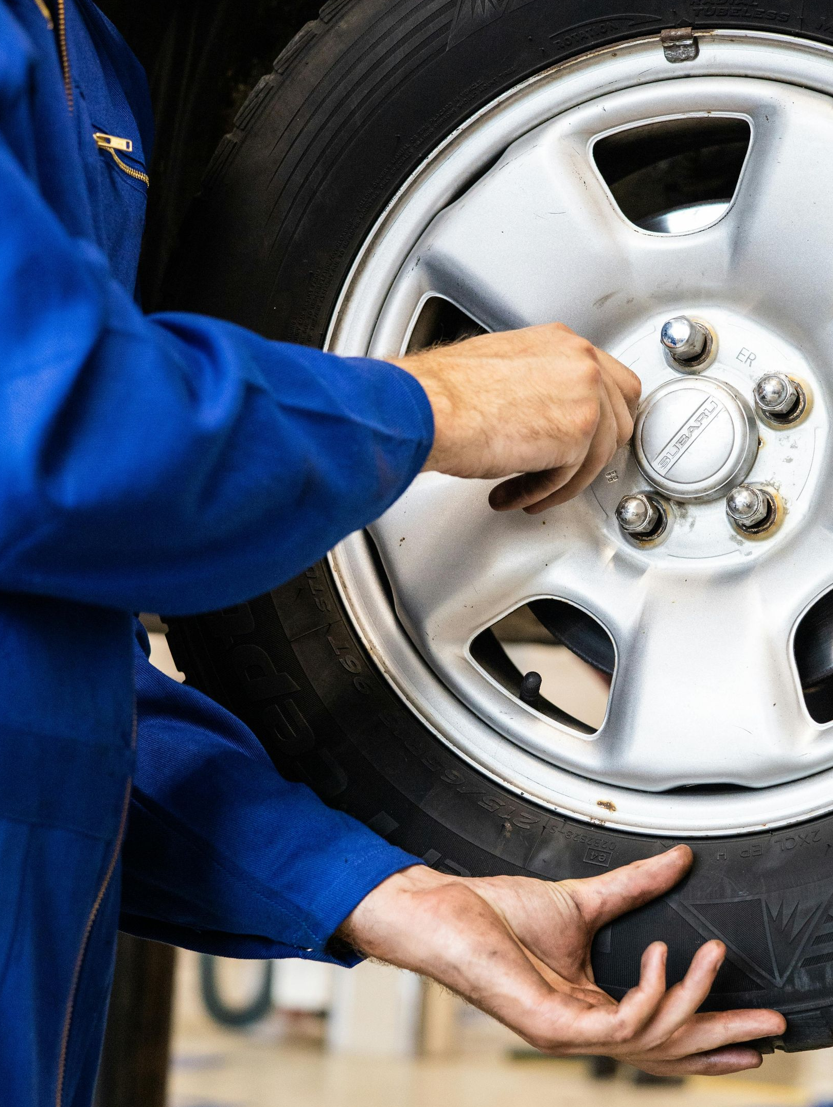 Person in blue jumpsuit working on a car tire, tightening lug nuts.