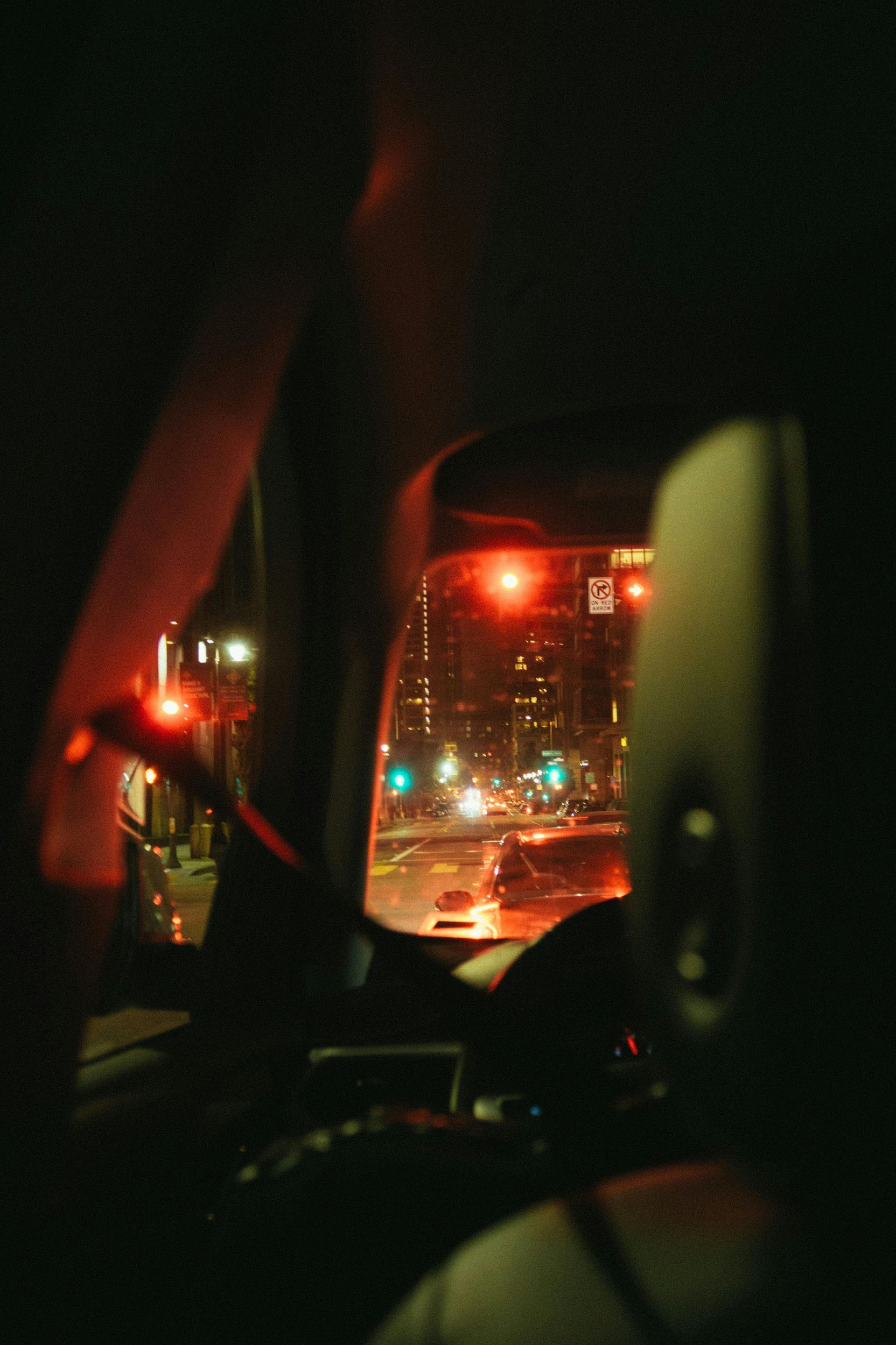 View from inside a car at night, looking at city lights. Red traffic lights glow.