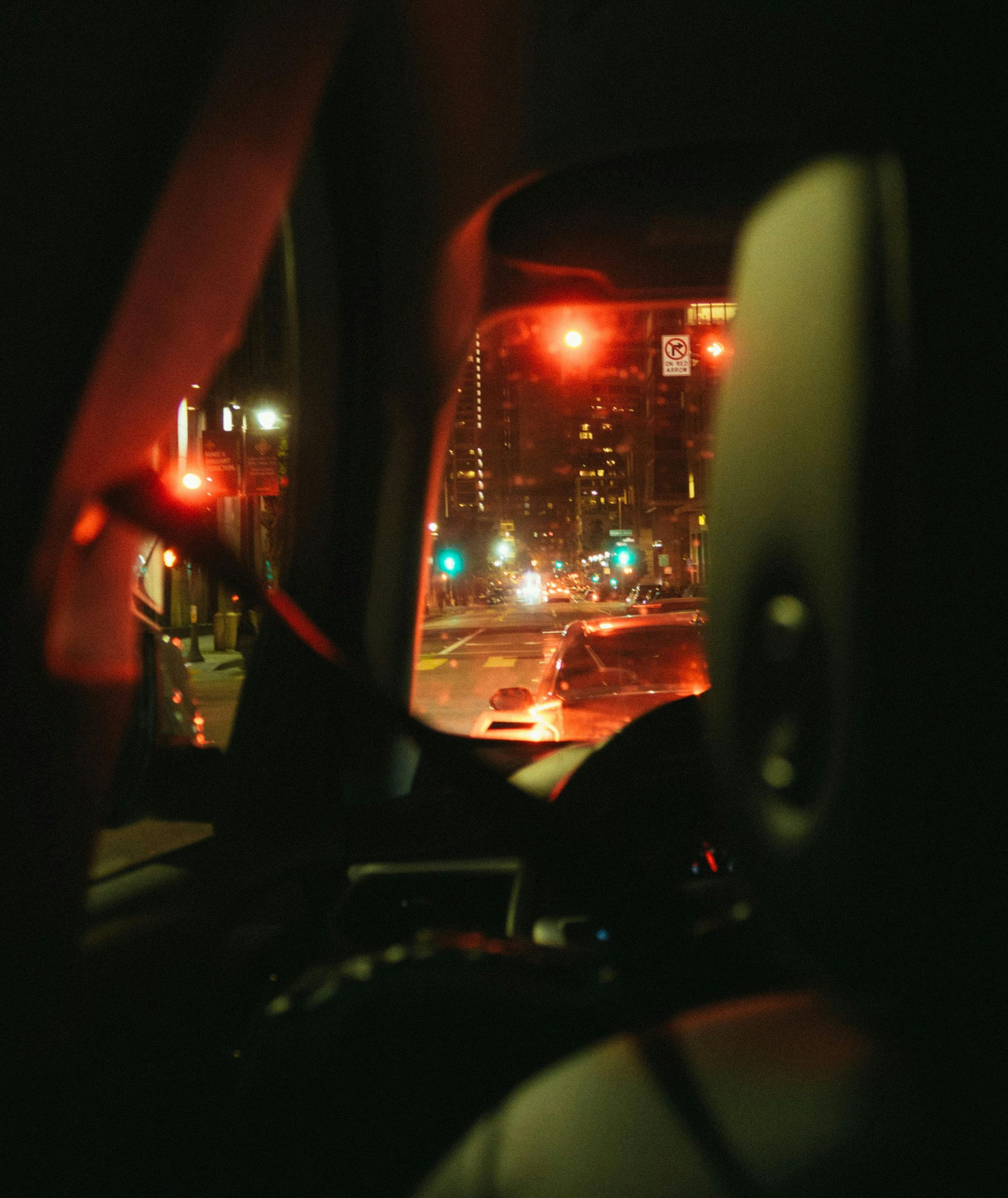 View from inside a car at night, looking at city lights. Red traffic lights glow.
