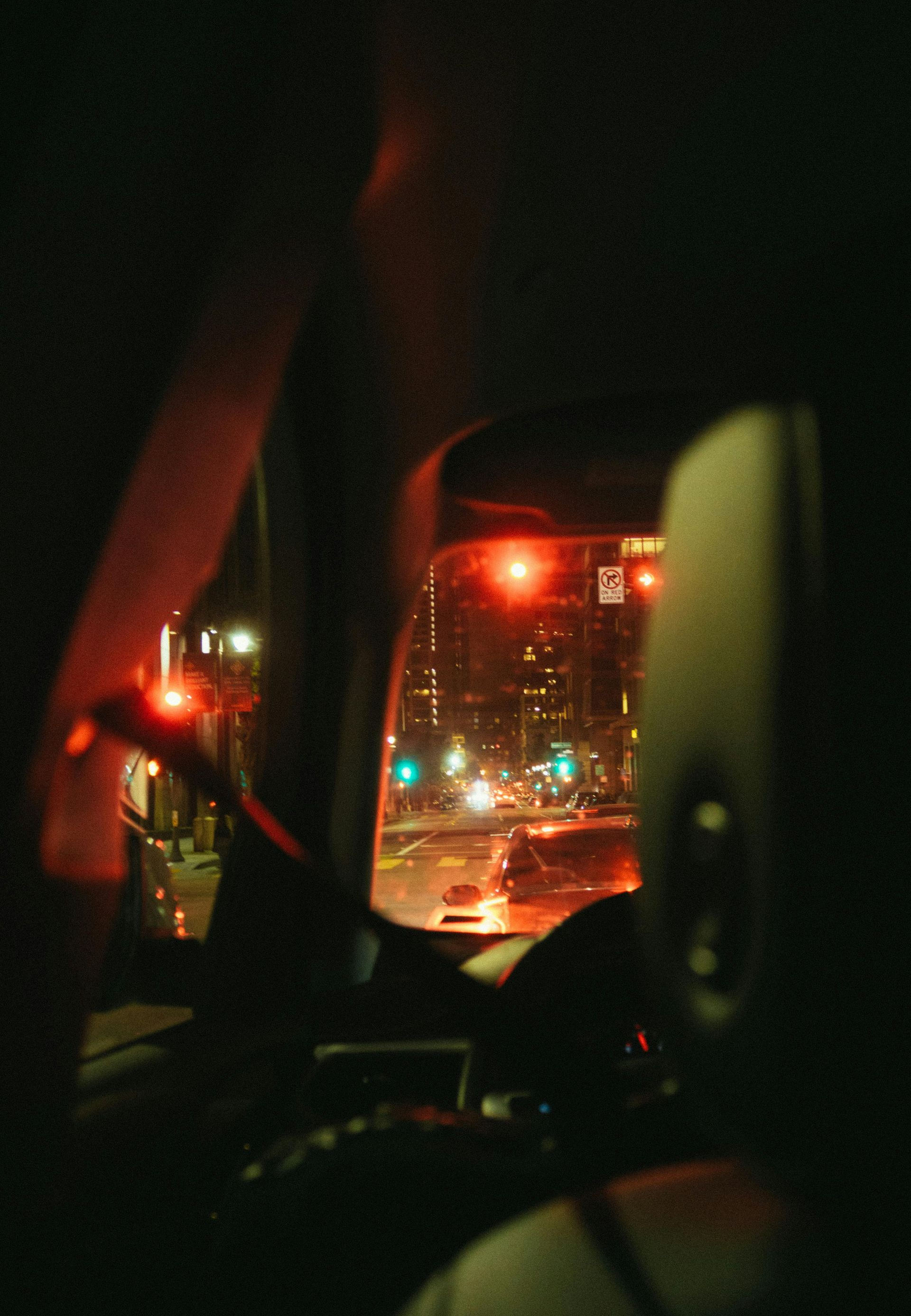View from inside a car at night, looking at city lights. Red traffic lights glow.