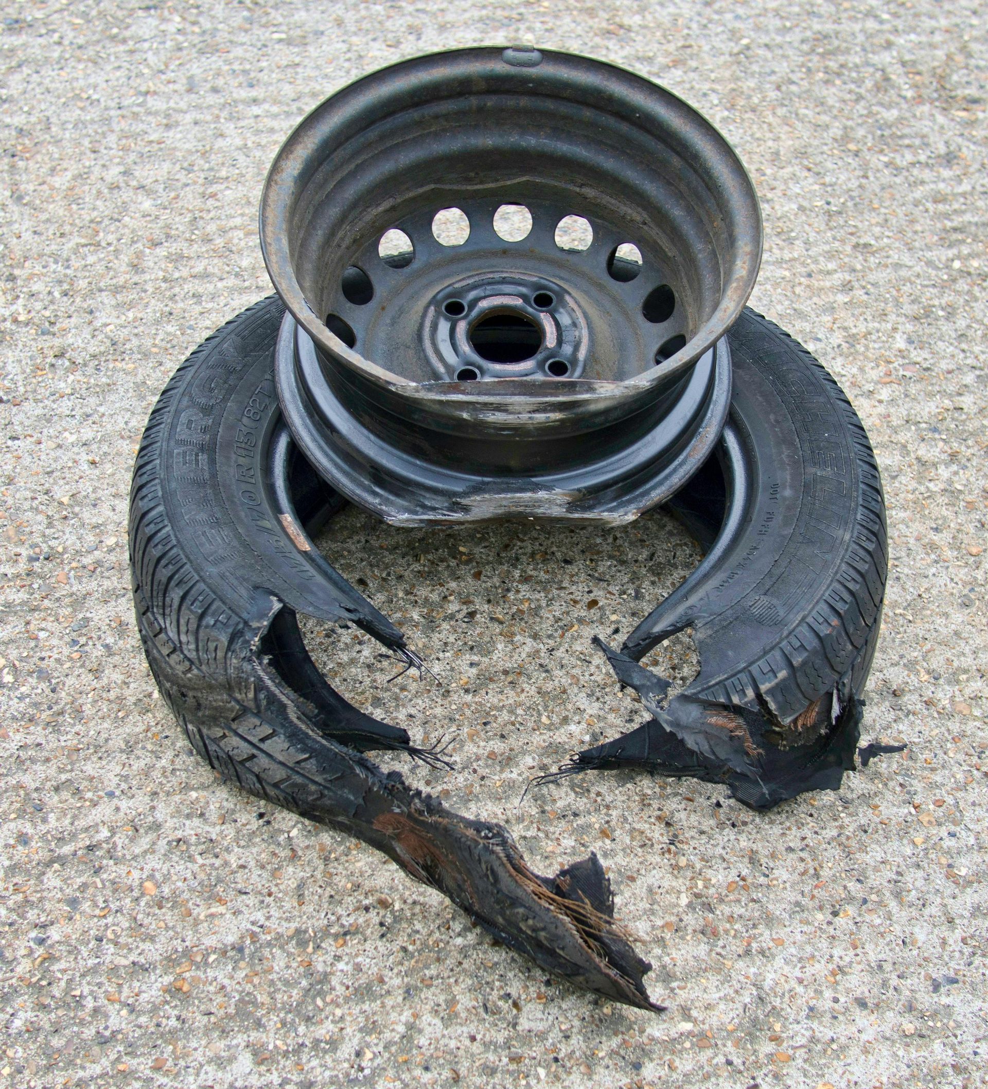 Damaged car tire and rim on concrete, with large tears in the tire and visible metal wheel.