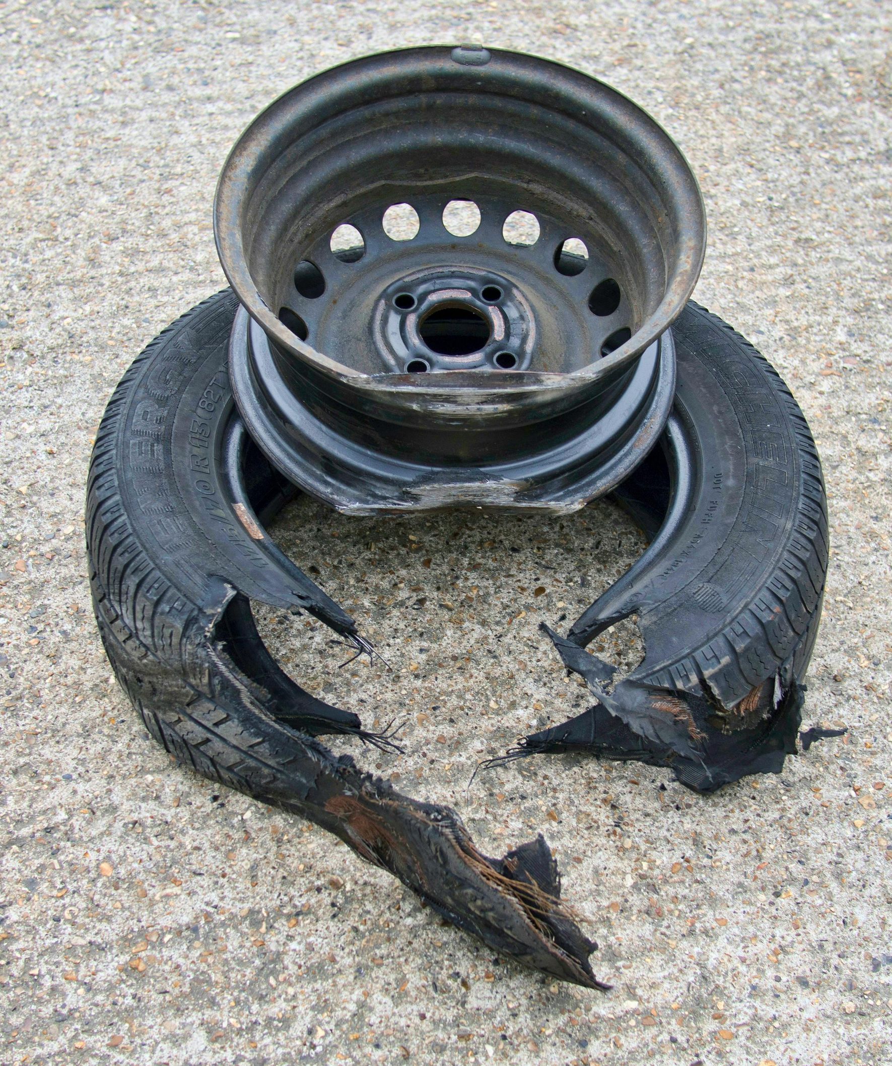 Damaged car tire and rim on pavement. The tire is torn apart, exposing the wheel.