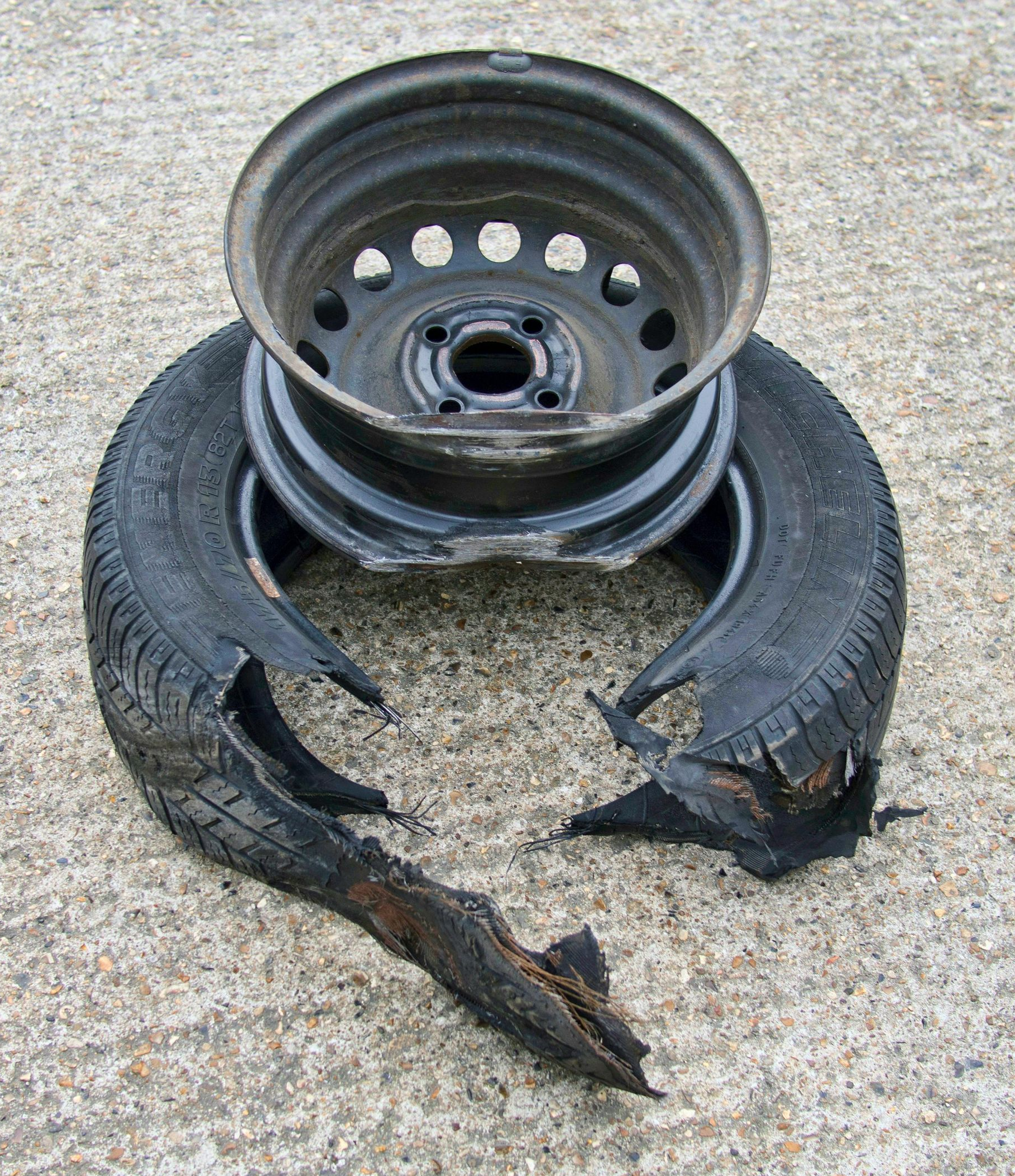 Damaged car tire and metal wheel on a concrete surface. Tire is split with detached pieces, wheel is dark.
