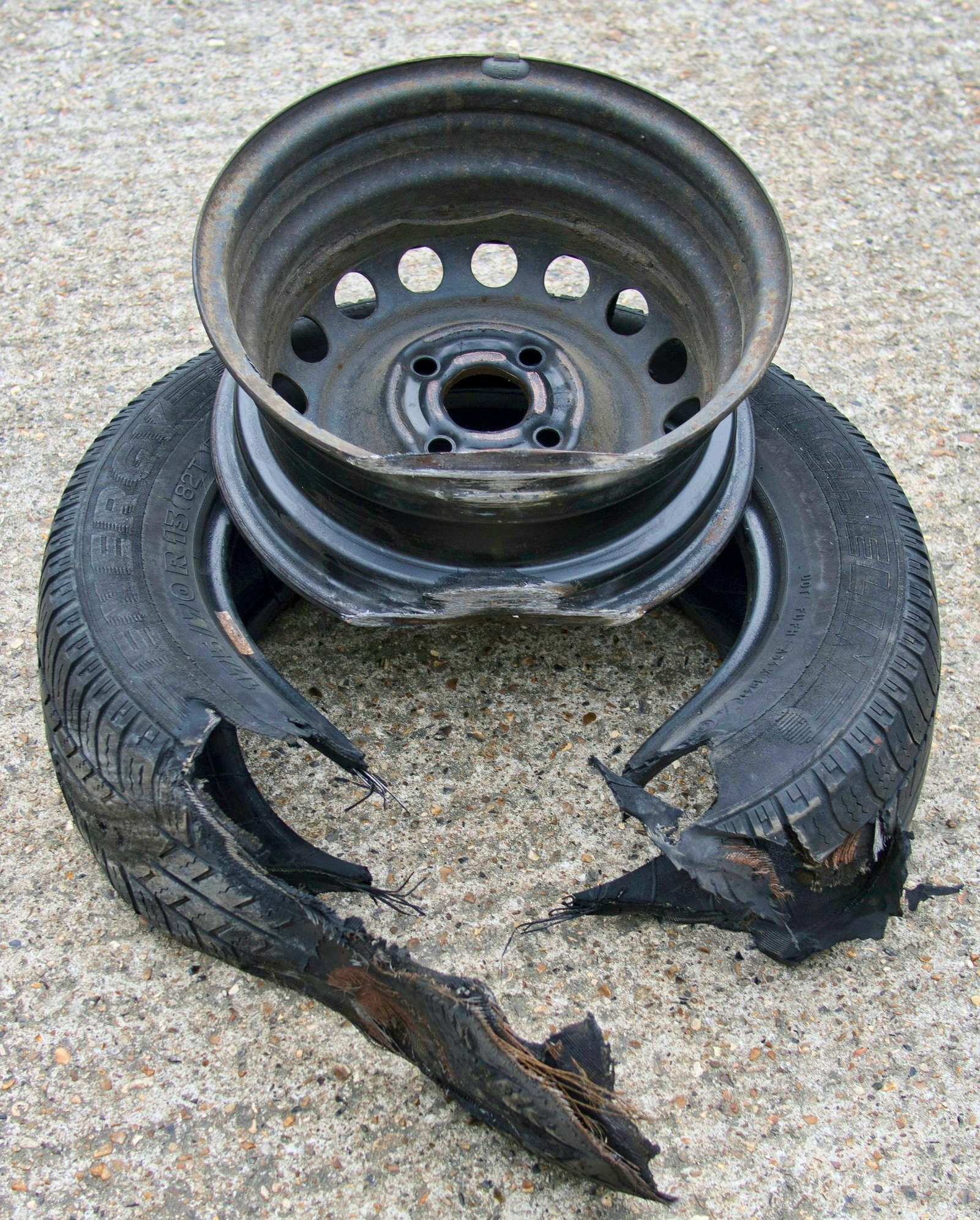 Damaged car tire and metal wheel on a concrete surface. Tire is split with detached pieces, wheel is dark.