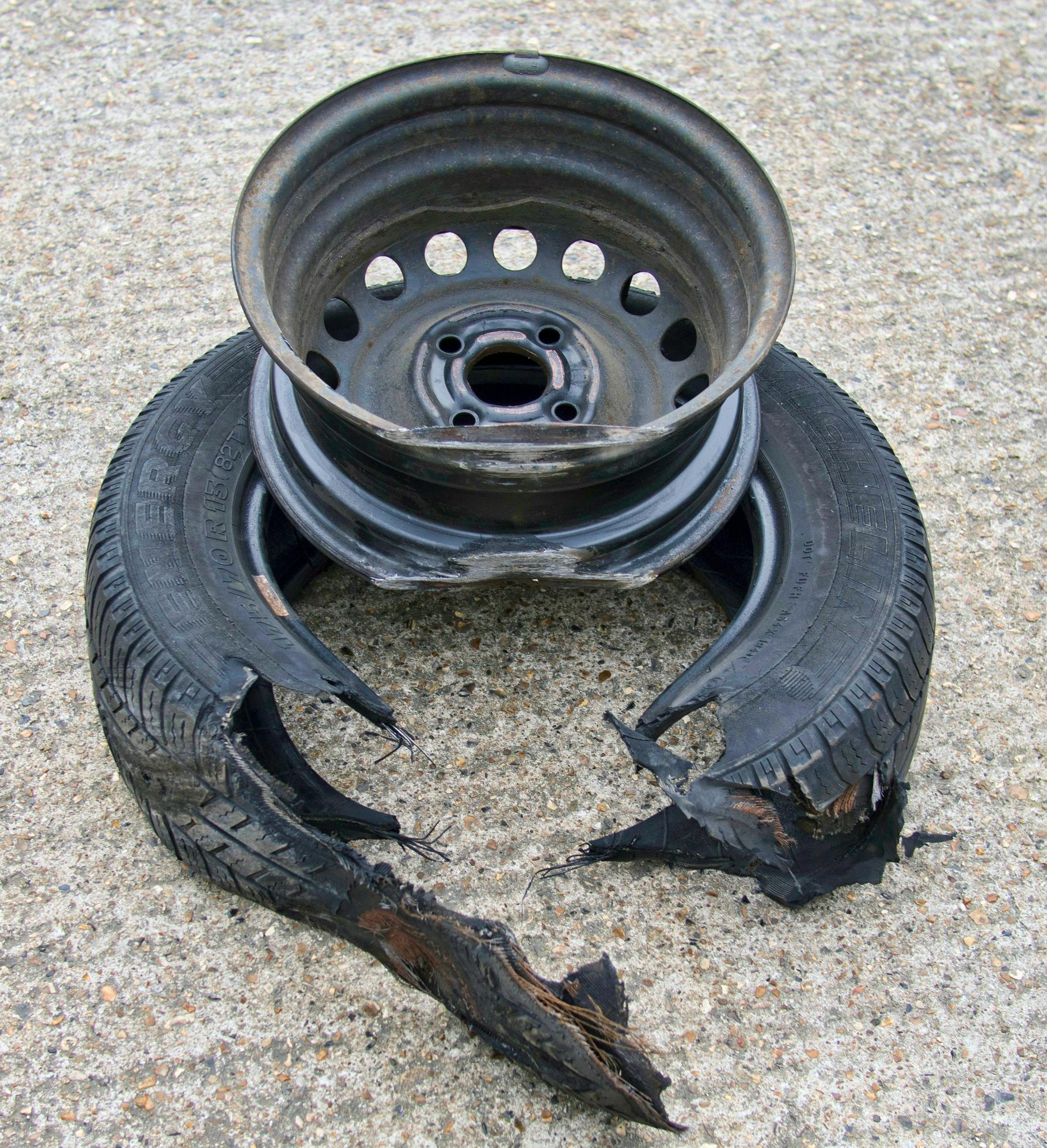 Damaged car tire and metal wheel on a concrete surface. Tire is split with detached pieces, wheel is dark.