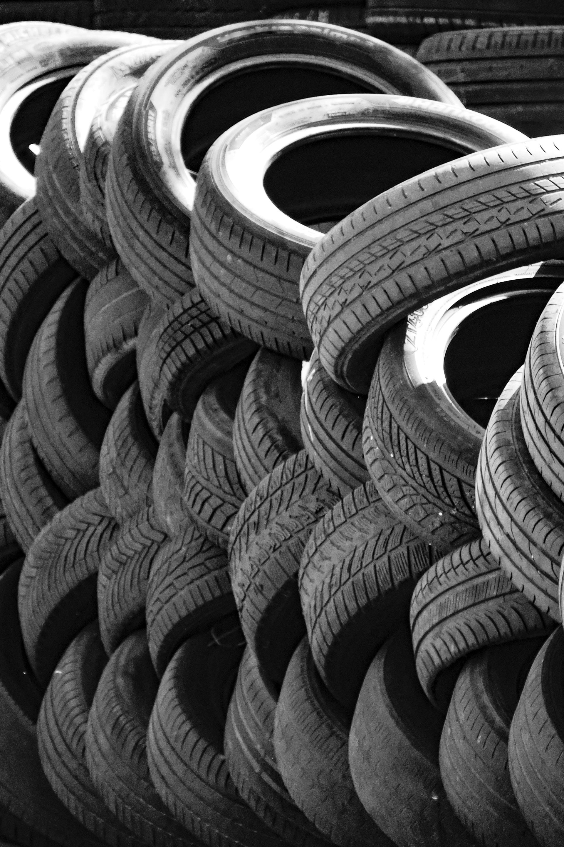A close-up, black and white shot of a large stack of used rubber tires piled together.
