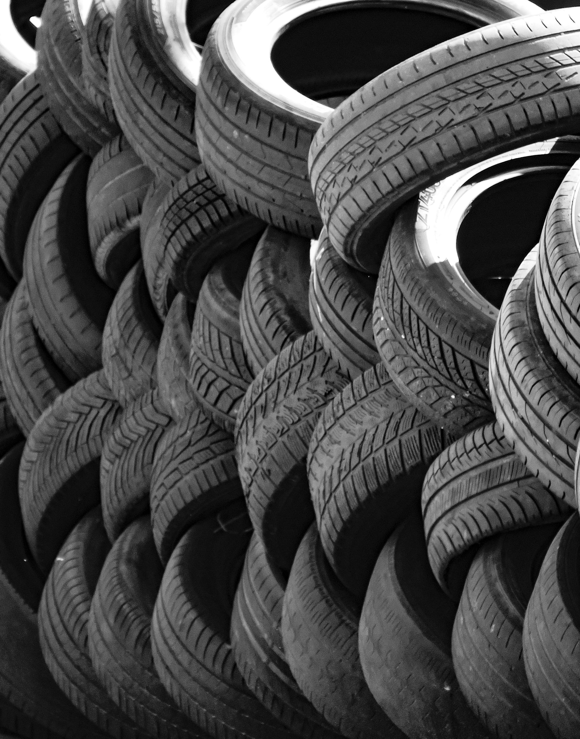 A close-up, black and white shot of a large stack of used rubber tires piled together.