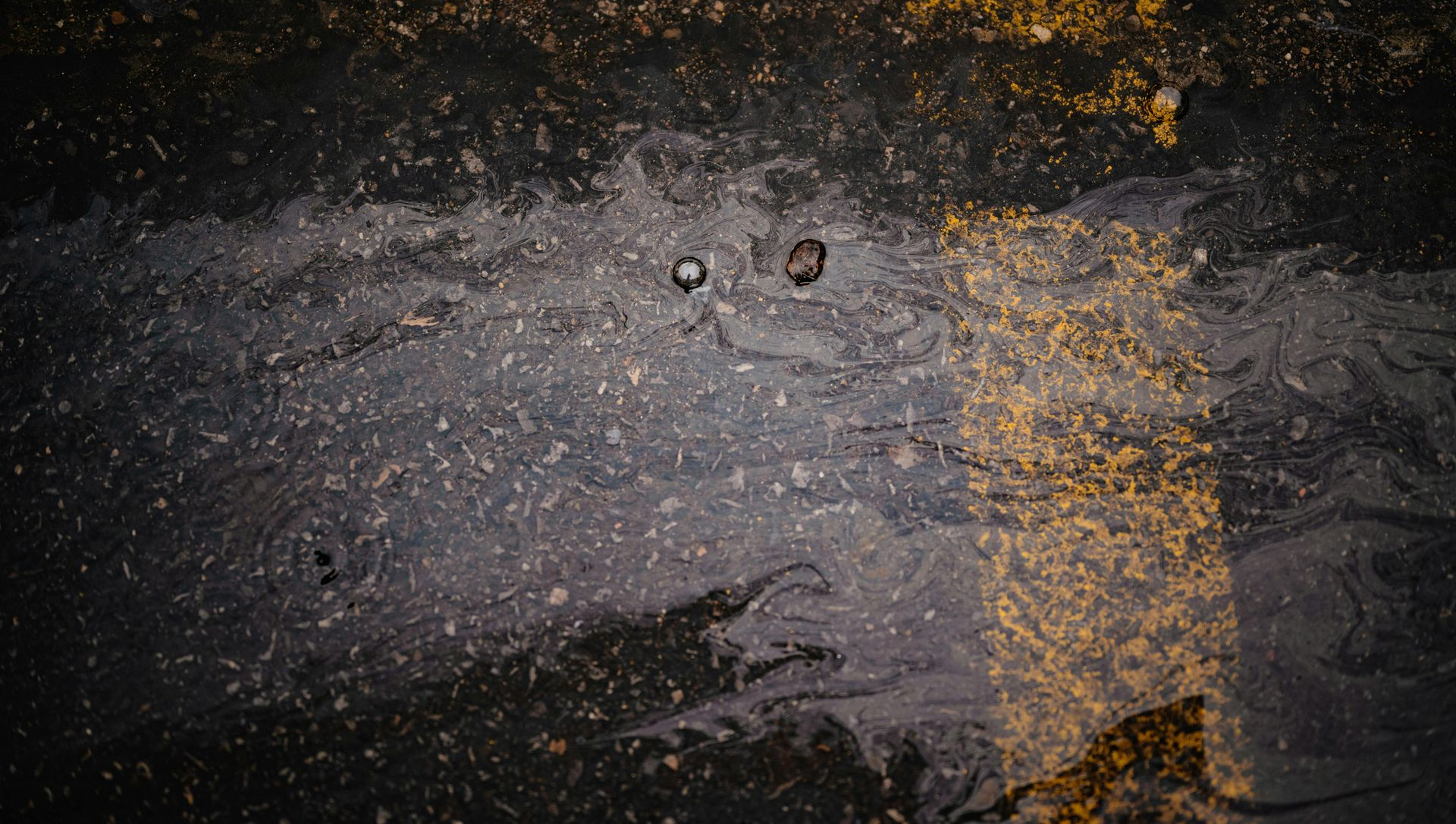 Close-up of asphalt road surface with yellow and white painted lines, two metal studs are visible.