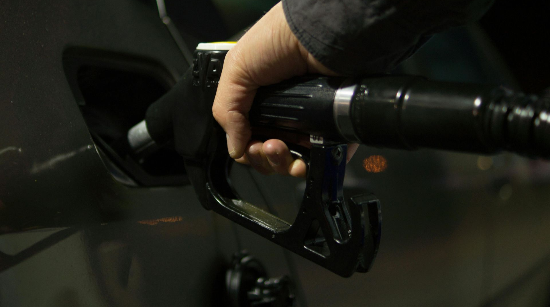Hand holding a gas pump nozzle filling a car's fuel tank.