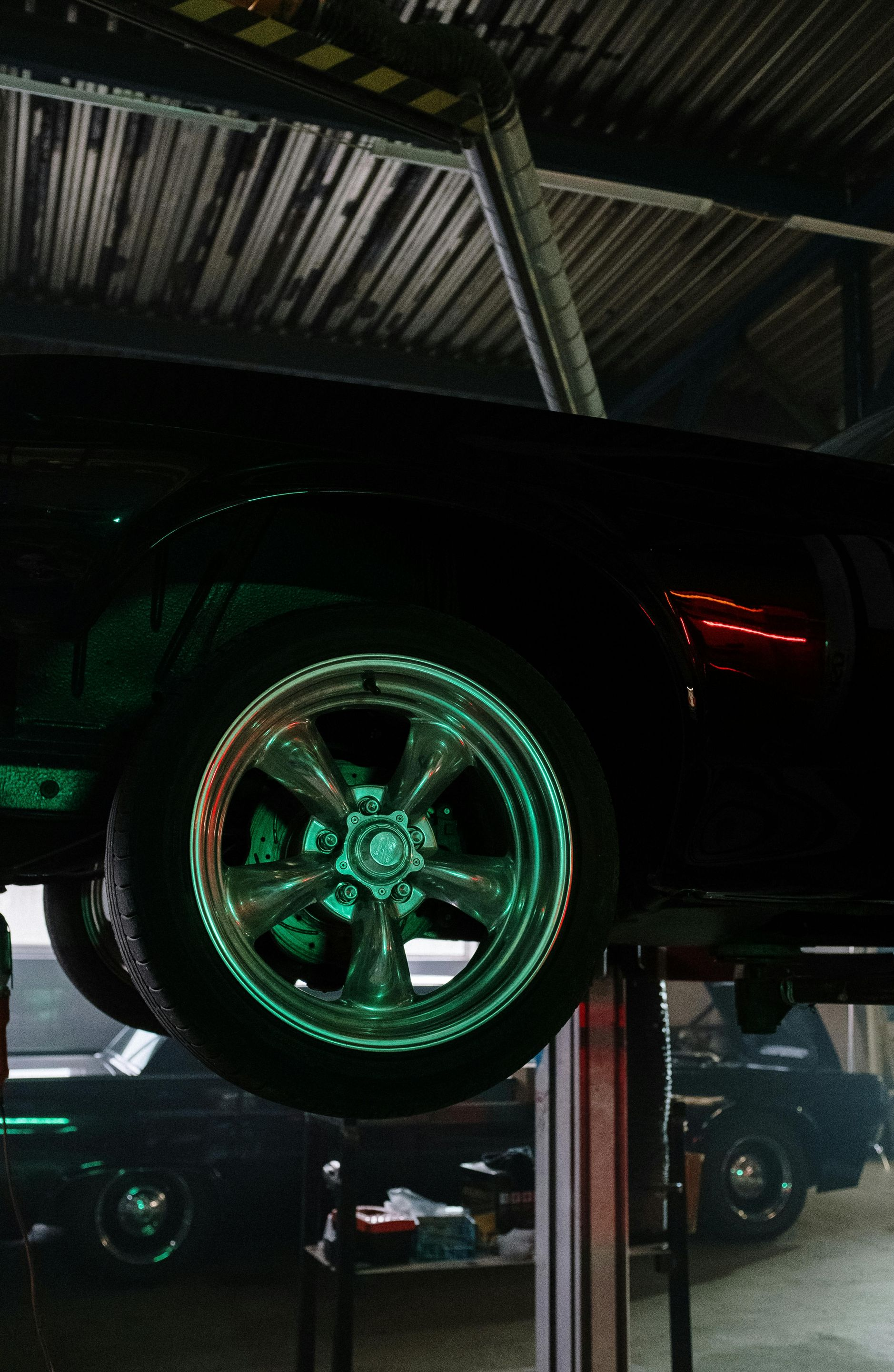 Black classic car raised on a lift in a garage, rims highlighted by green light.