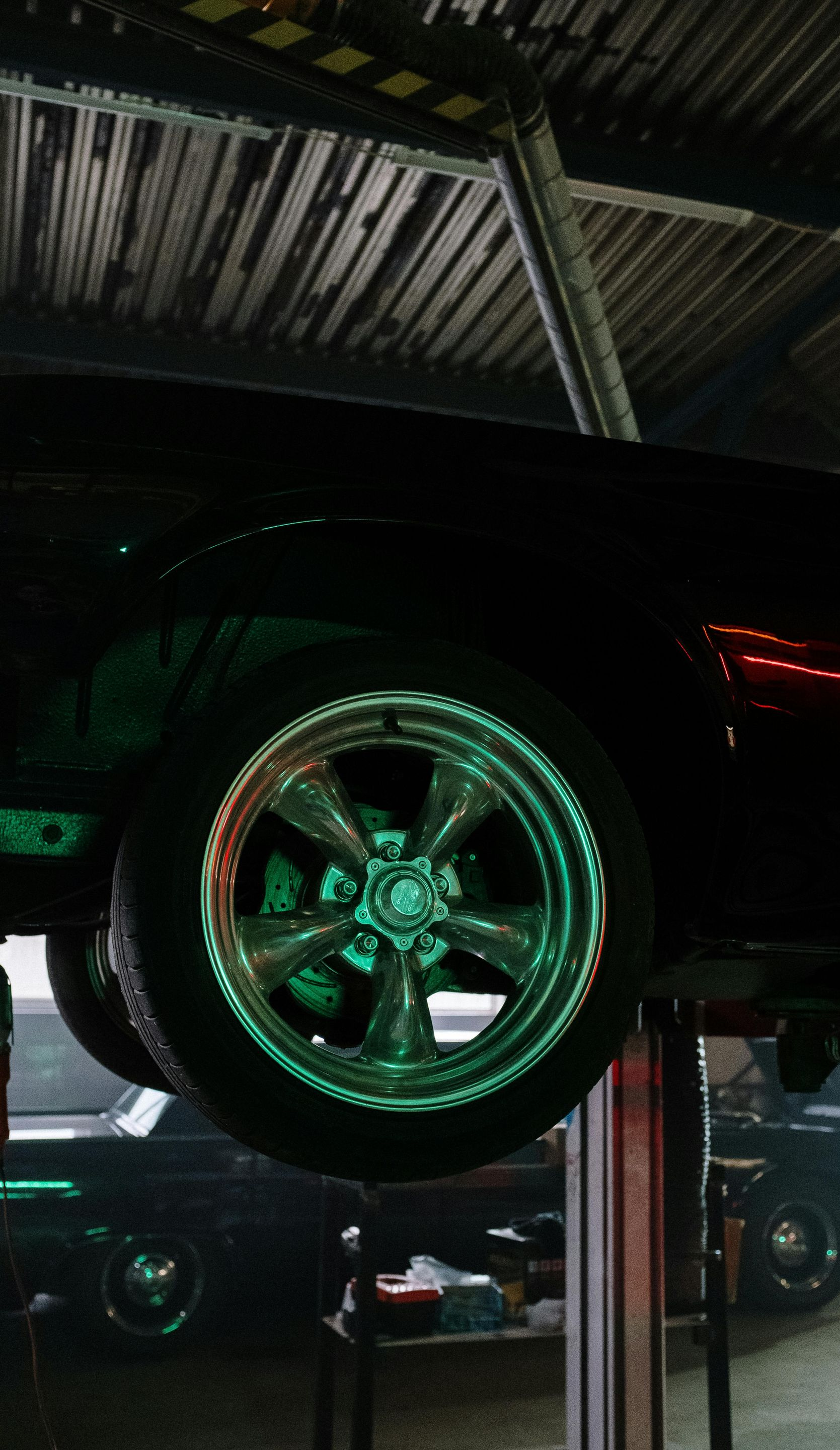 Black classic car raised on a lift in a garage, rims highlighted by green light.