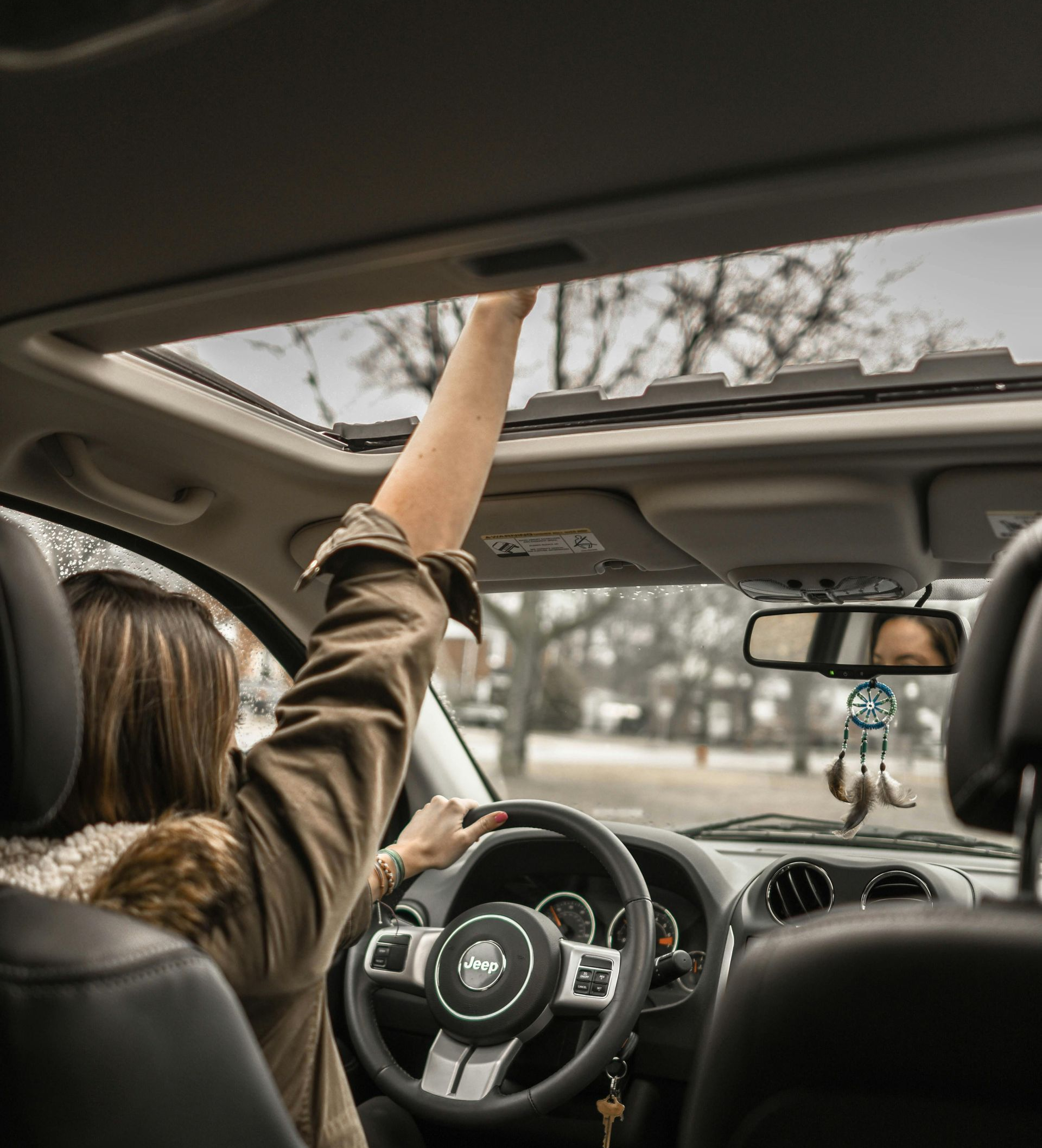 Person reaching out of a car's sunroof, hand in the air. Driving with the steering wheel visible.