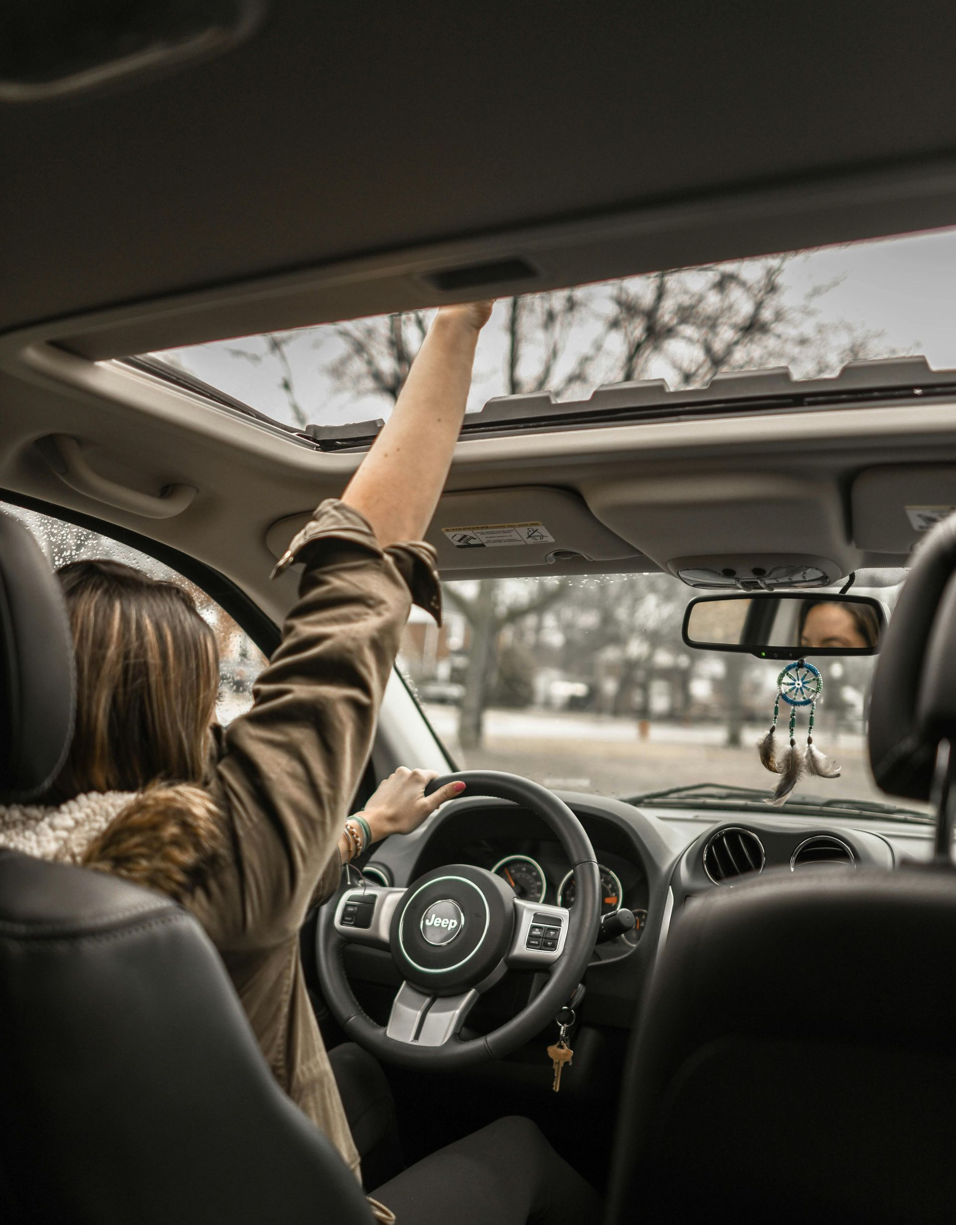 Person reaching out of a car's sunroof, hand in the air. Driving with the steering wheel visible.