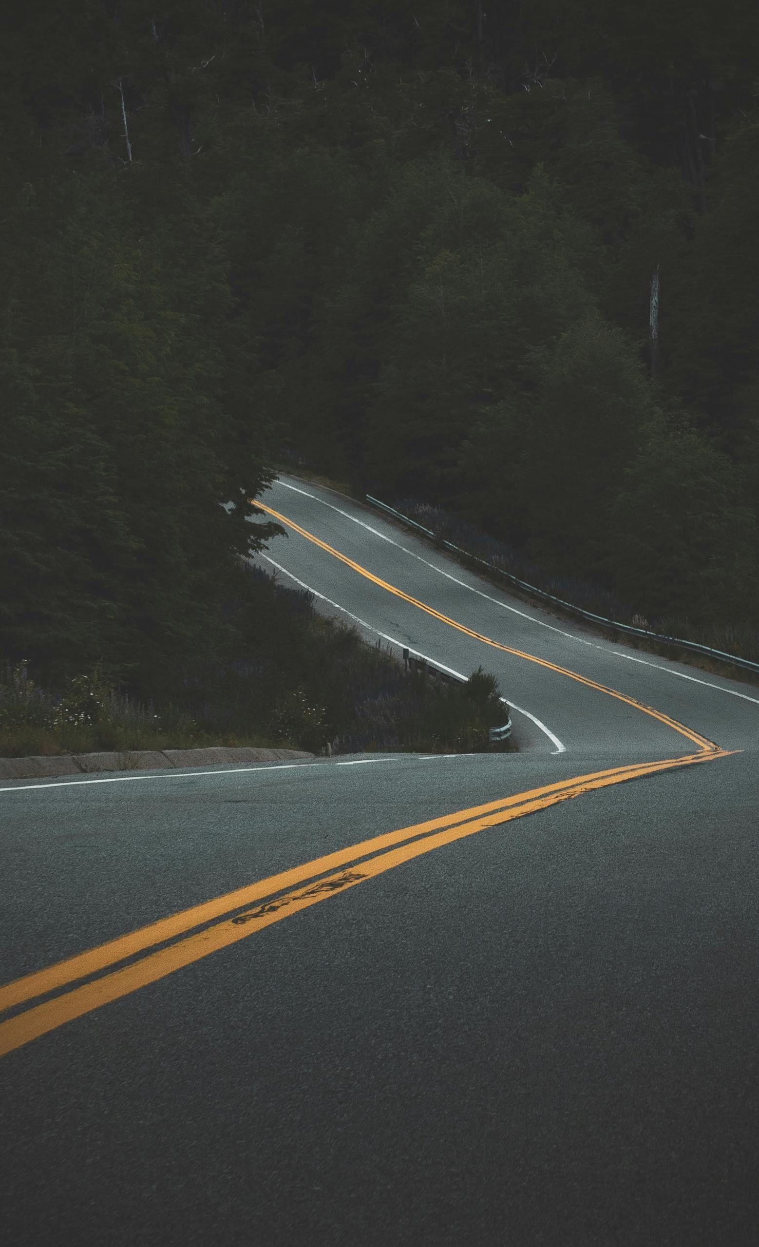 A car is driving down a curvy road with yellow lines.
