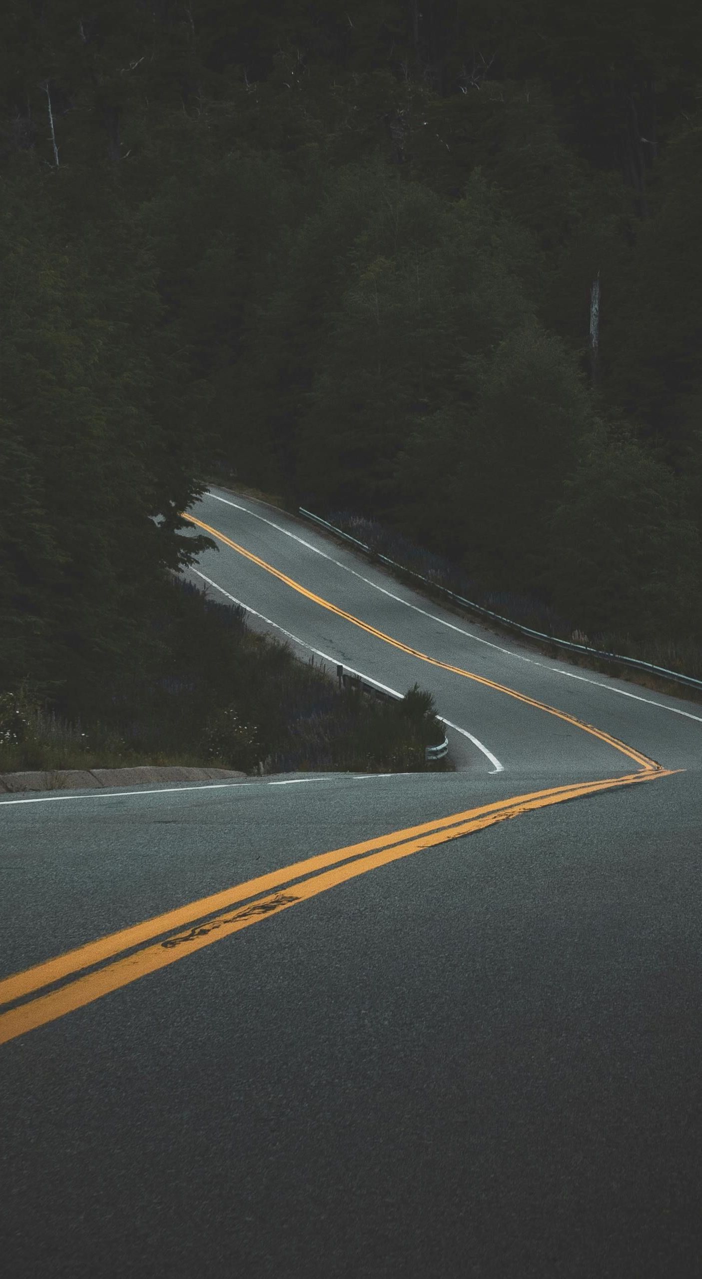A car is driving down a curvy road with yellow lines.