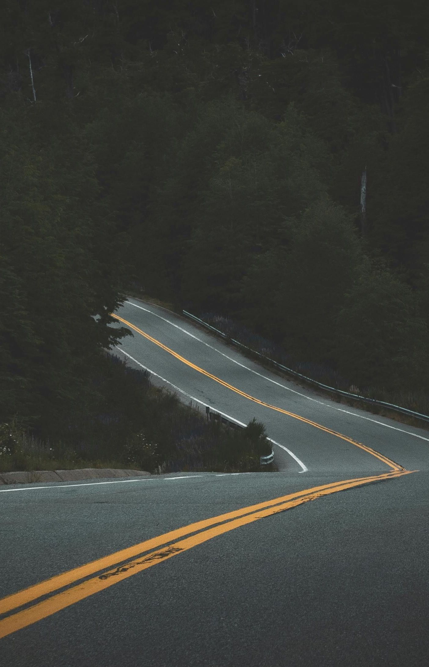 A car is driving down a curvy road with yellow lines.