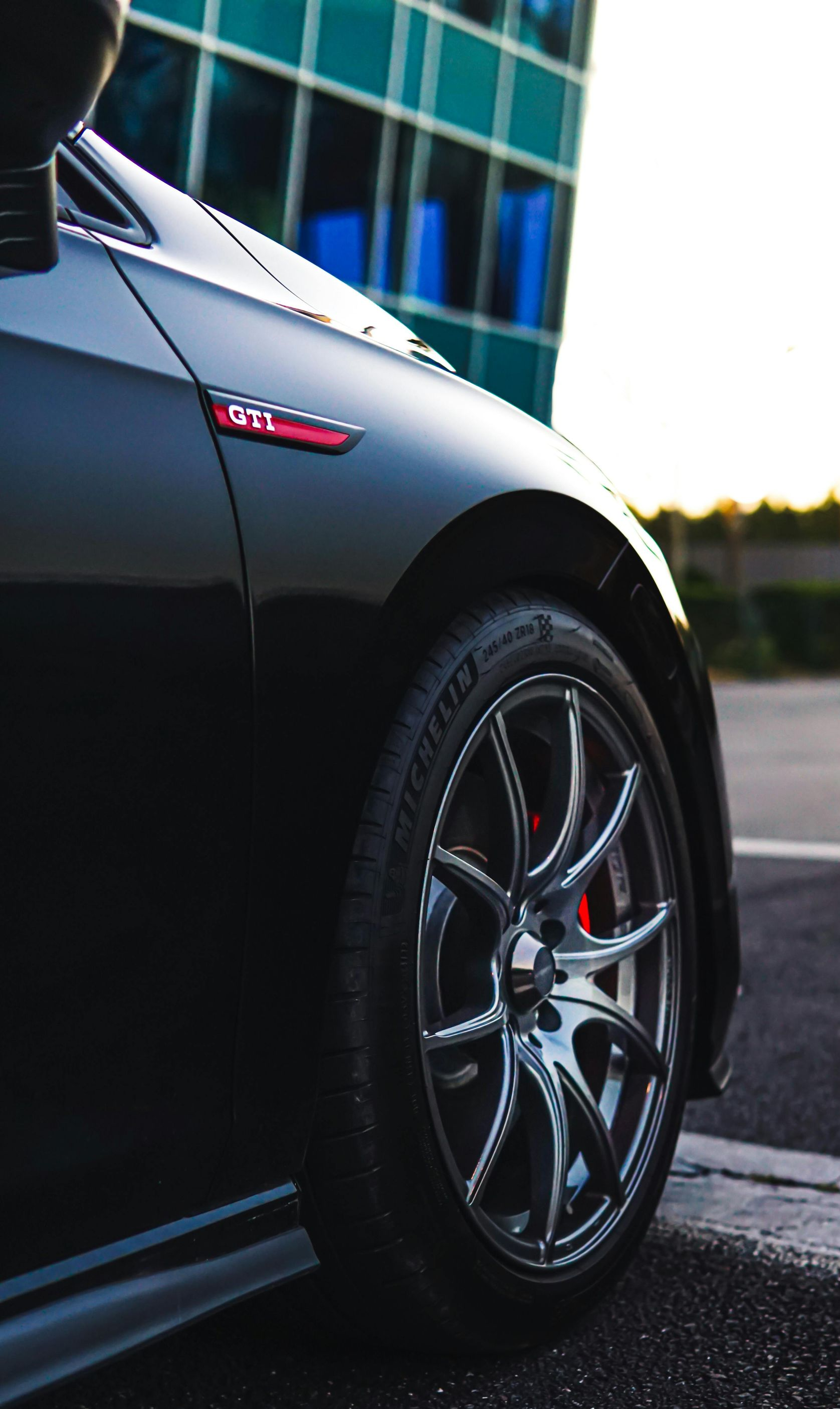 Black VW GTI car with red brake calipers, side view, parked near a building.