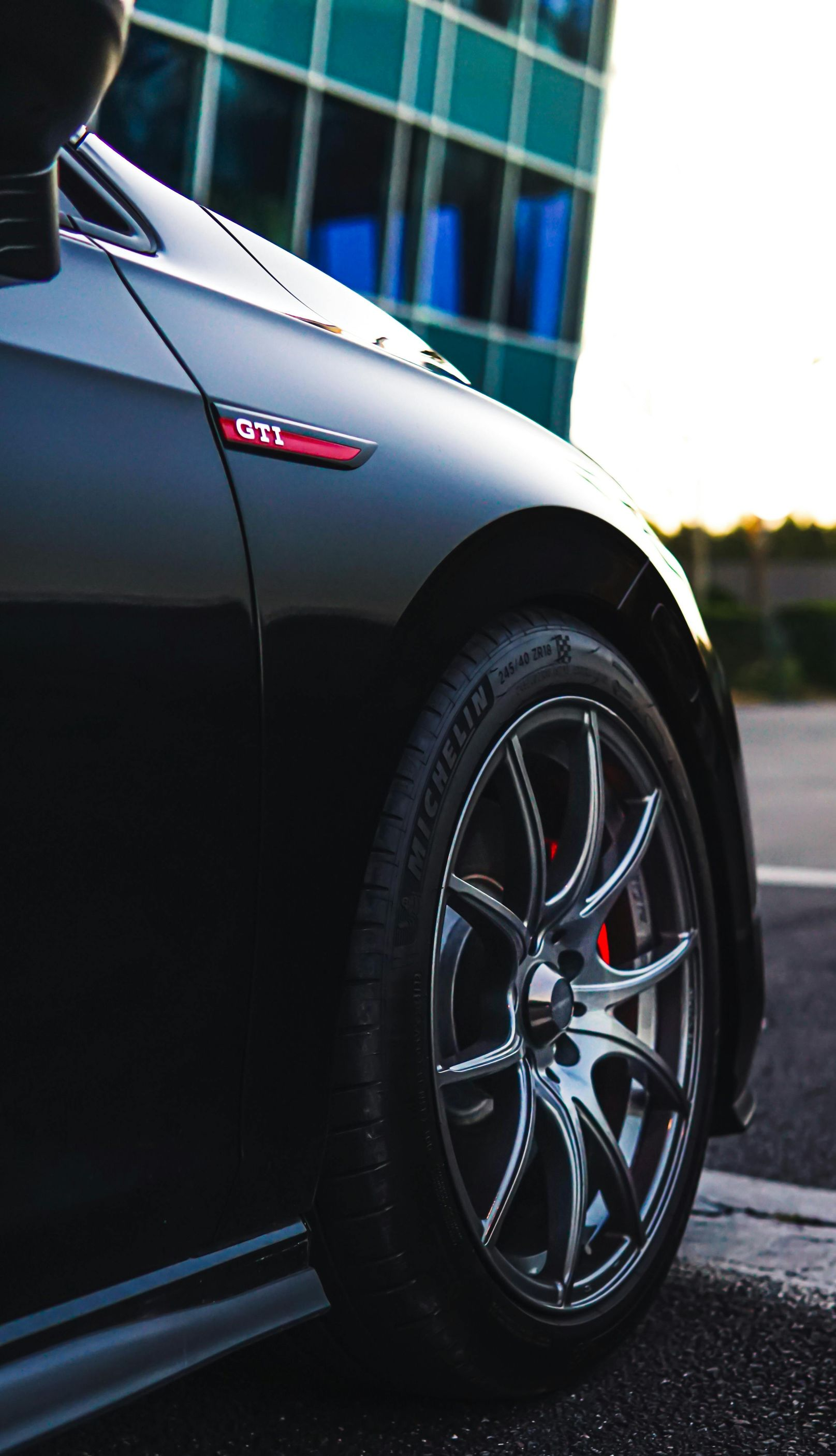 Black VW GTI car with red brake calipers, side view, parked near a building.