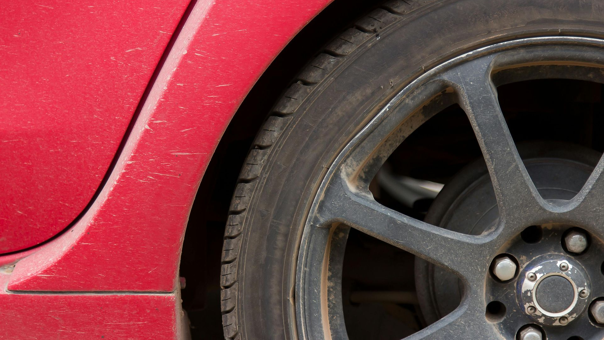 Red car's front tire and rim, covered in dirt.