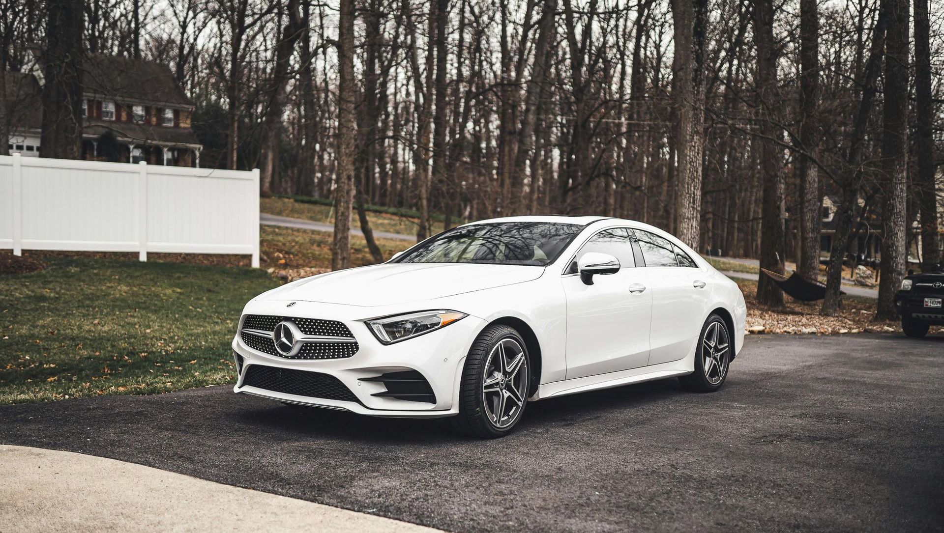 White Mercedes sedan parked on a driveway with a house and trees in the background.