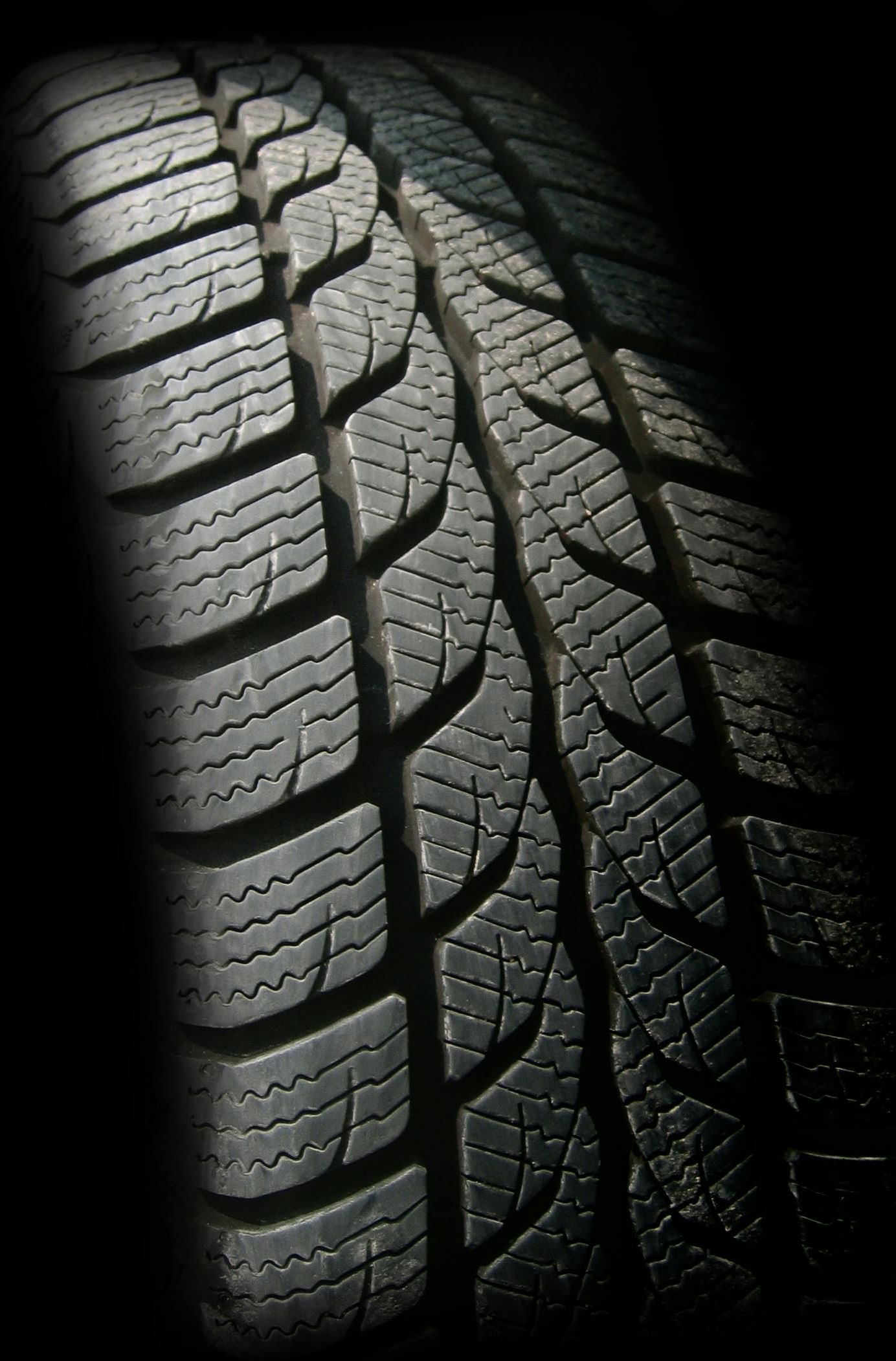 Close-up of a tire with a deeply grooved tread pattern, partially lit and set against a dark background.