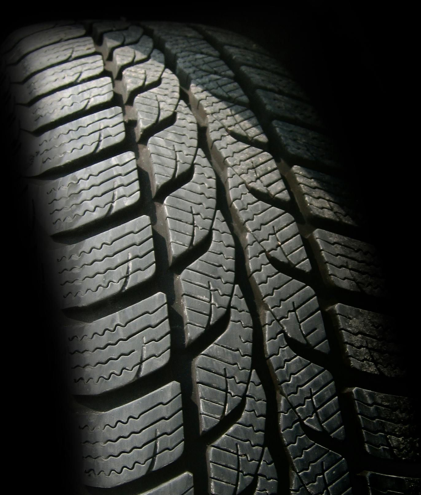 Close-up of a tire with a deeply grooved tread pattern, partially lit and set against a dark background.
