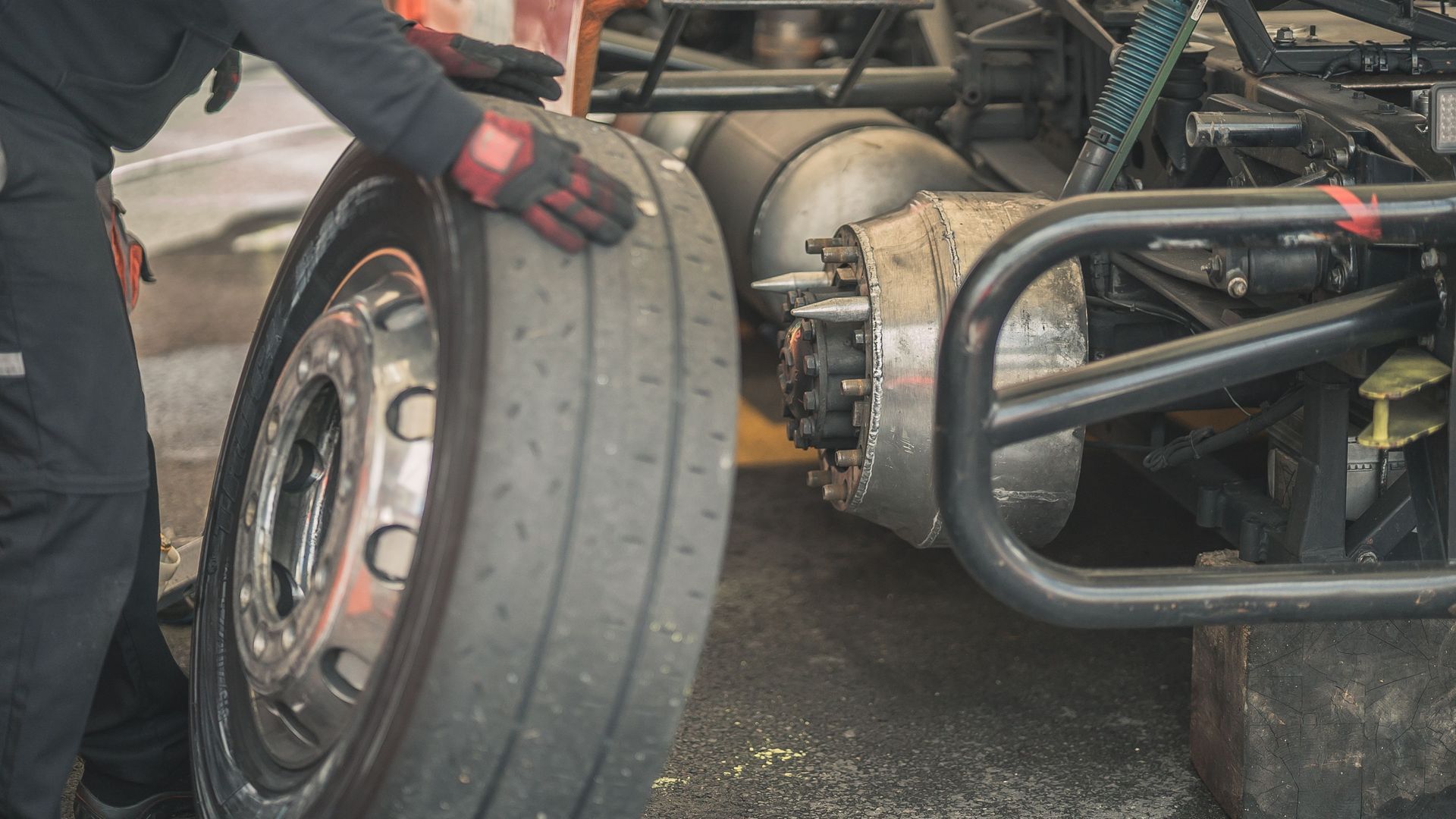Person in gloves adjusting a large racing tire on a damaged race car in a garage.