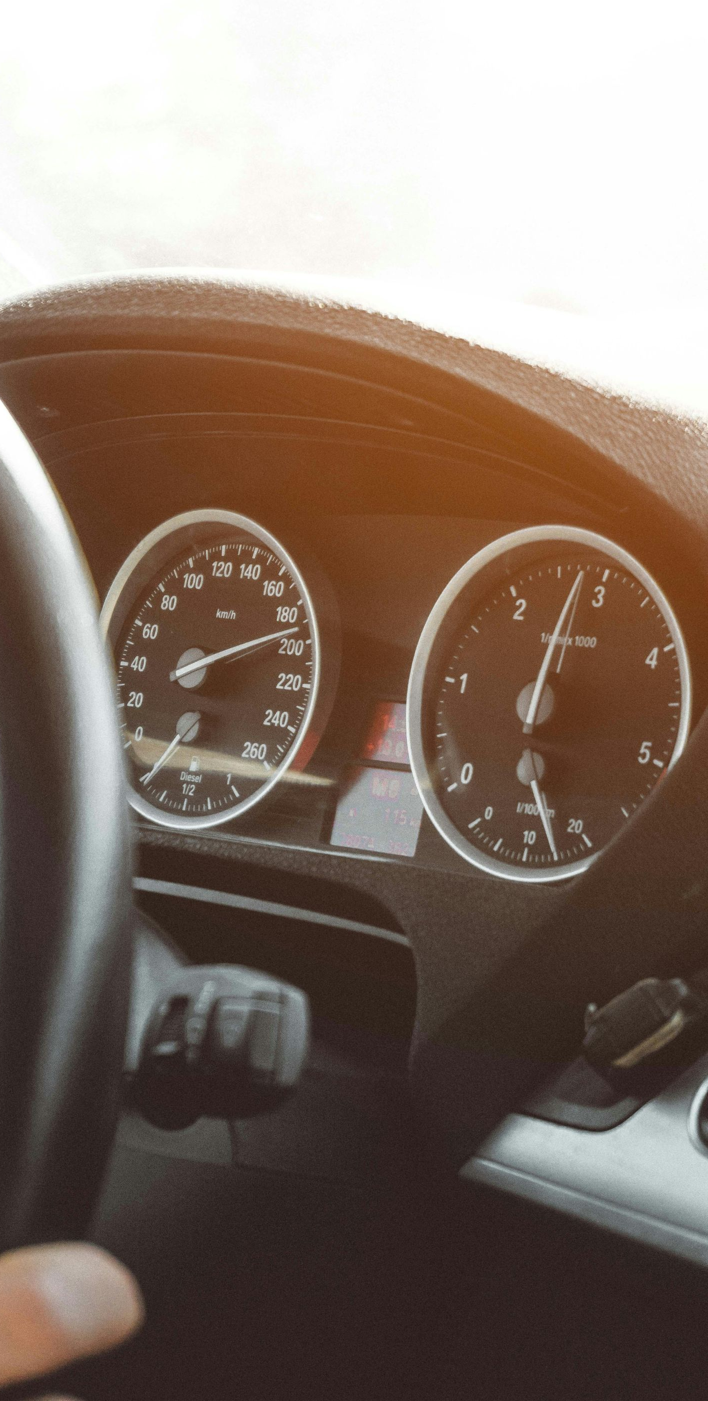 Dashboard of a car with a hand on the steering wheel, gauges visible. Sunlight shines.