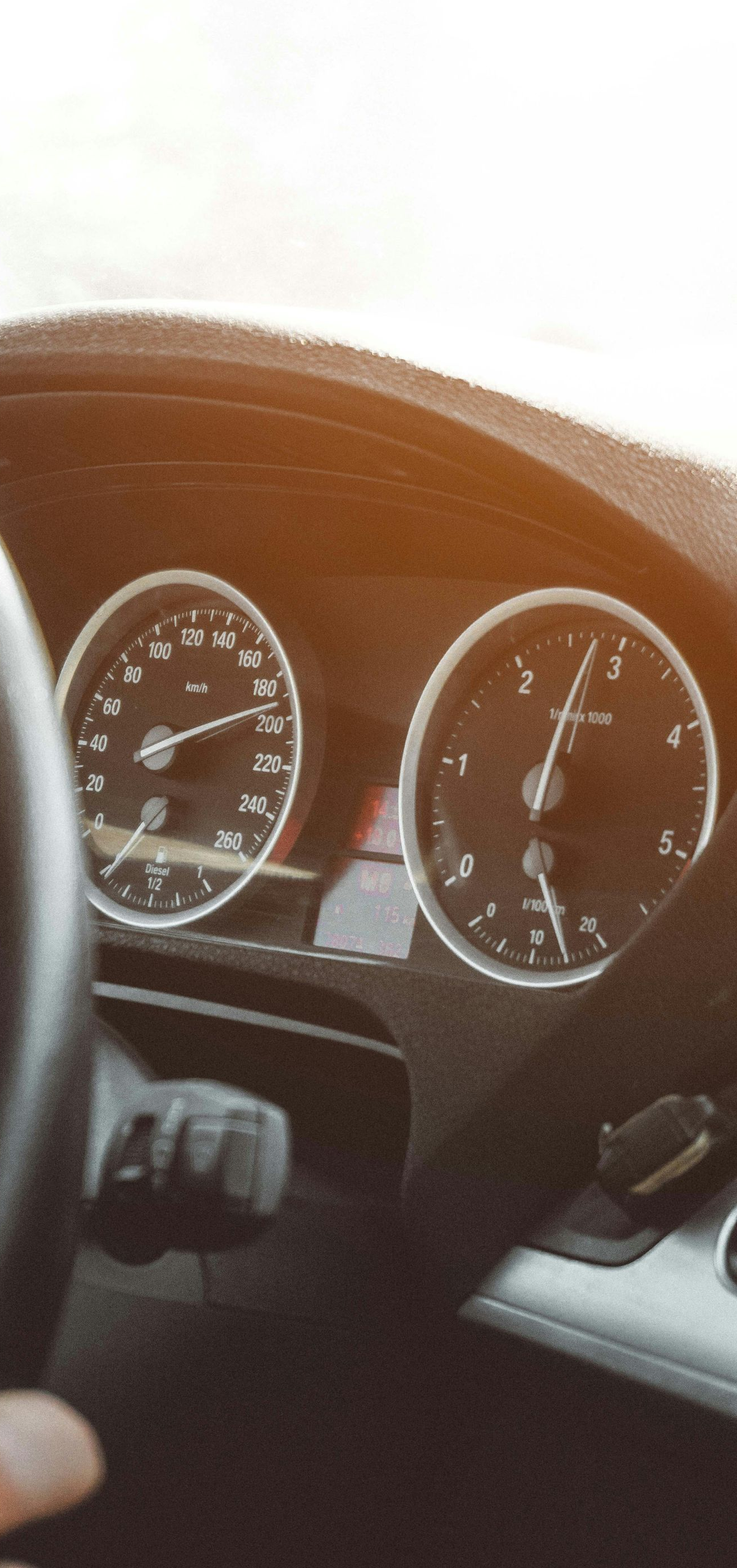Dashboard of a car with a hand on the steering wheel, gauges visible. Sunlight shines.