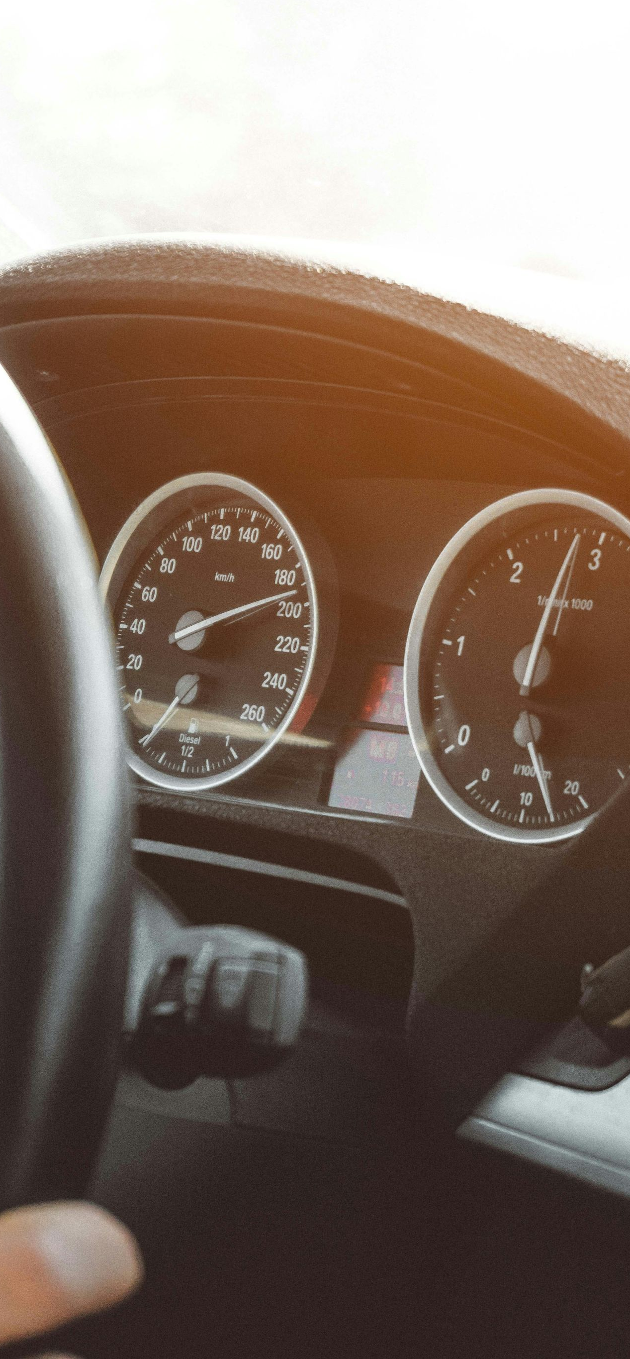 Dashboard of a car with a hand on the steering wheel, gauges visible. Sunlight shines.