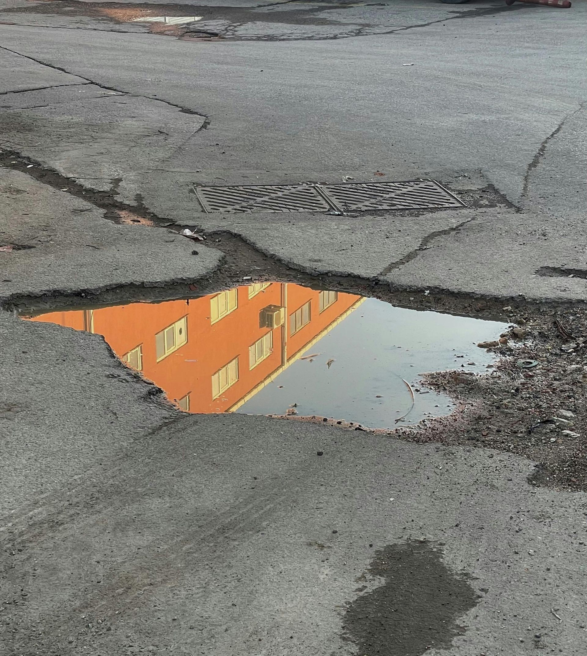 Puddle reflecting a bright orange building with windows on cracked asphalt.