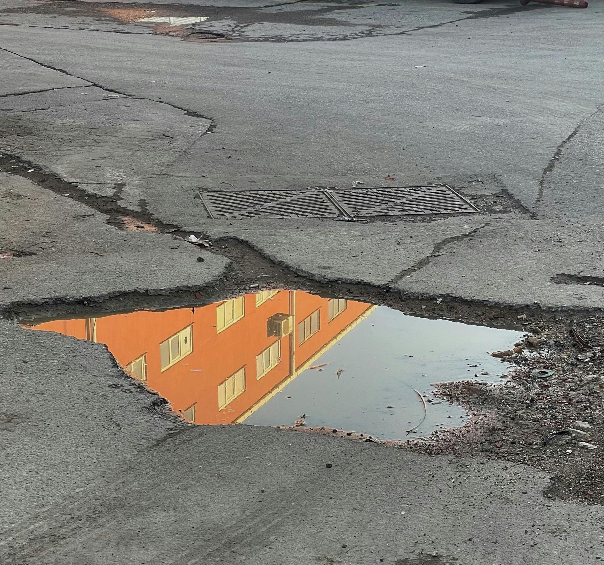 Puddle reflecting a bright orange building with windows on cracked asphalt.