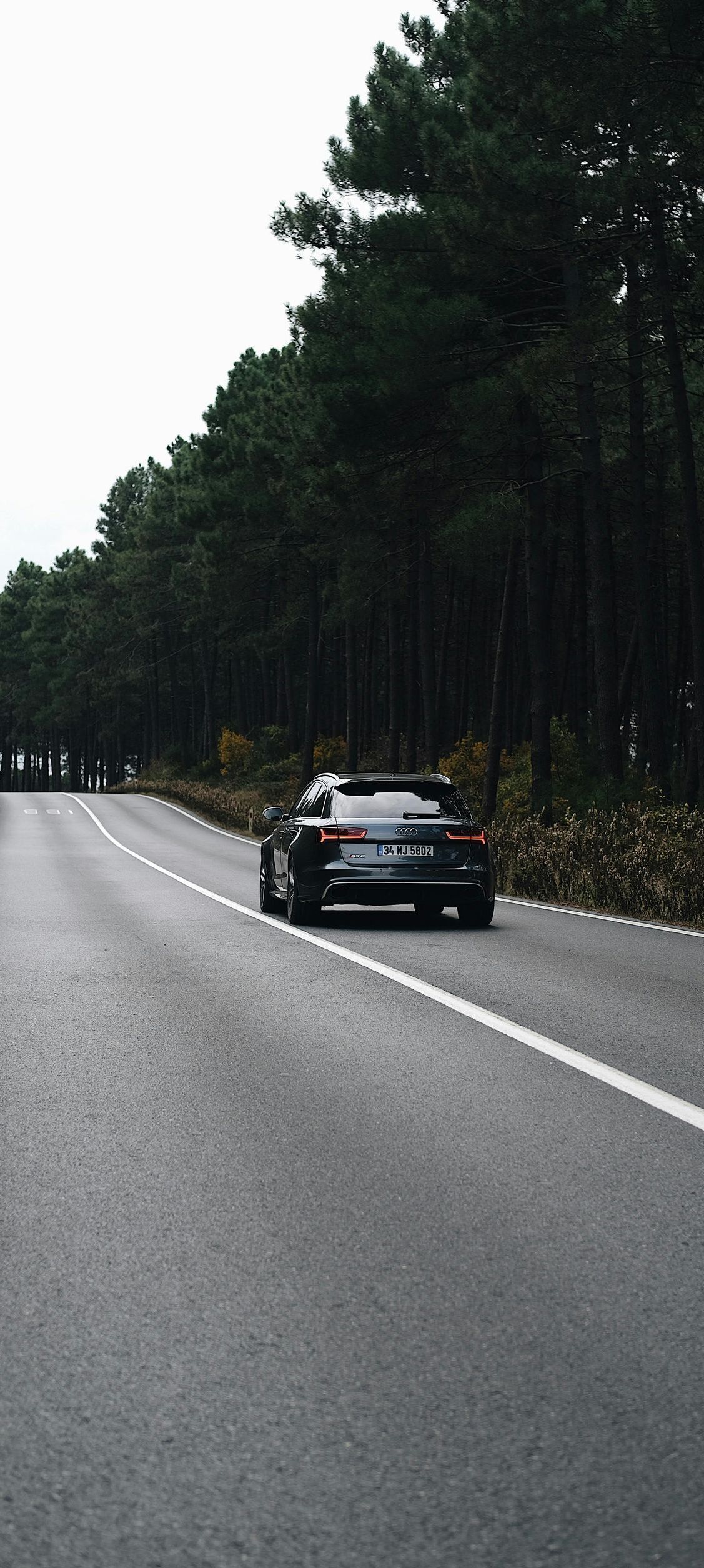 A car is driving down a road next to a forest.