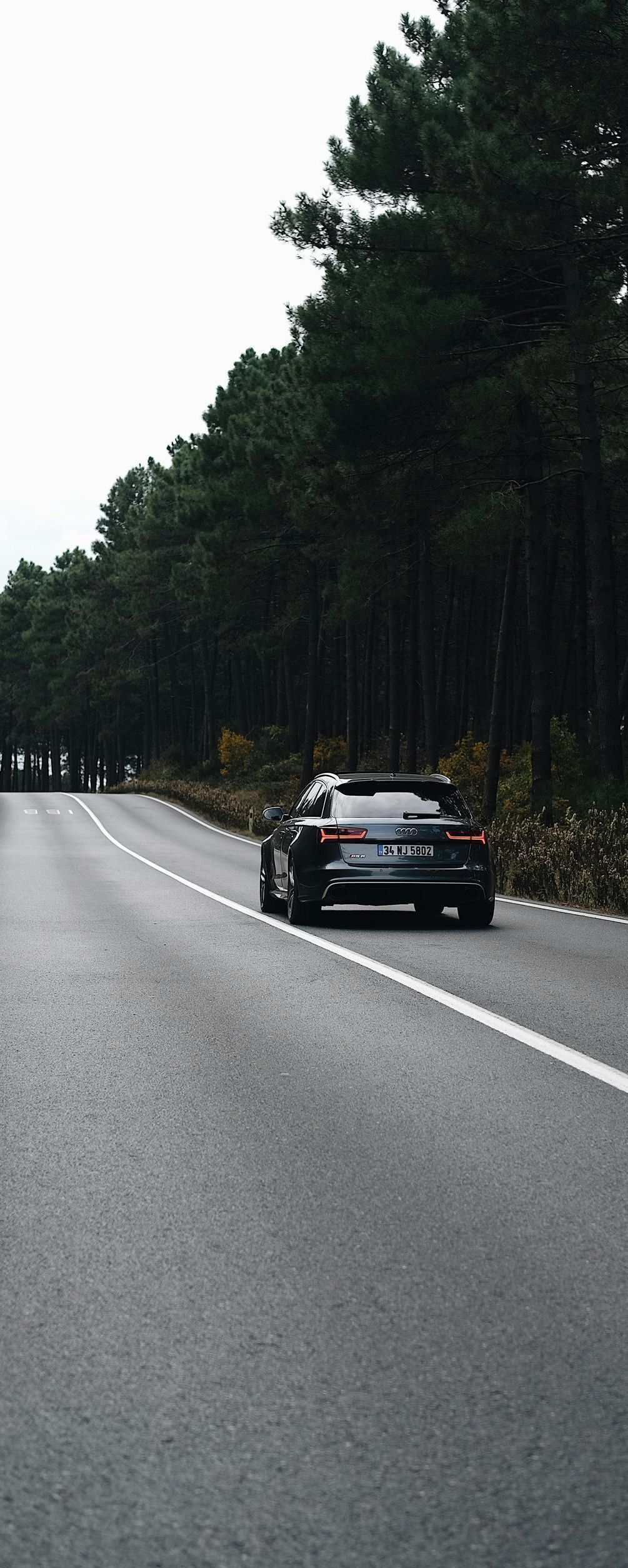 A car is driving down a road next to a forest.