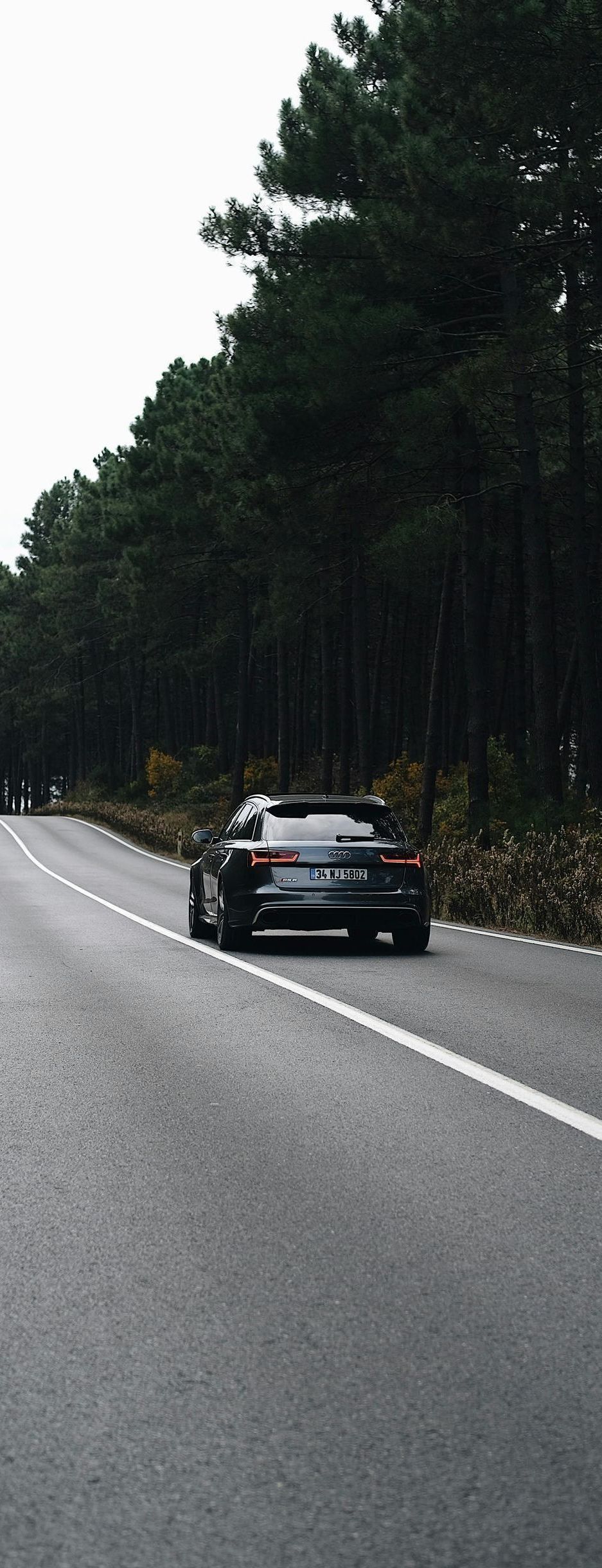 A car is driving down a road next to a forest.